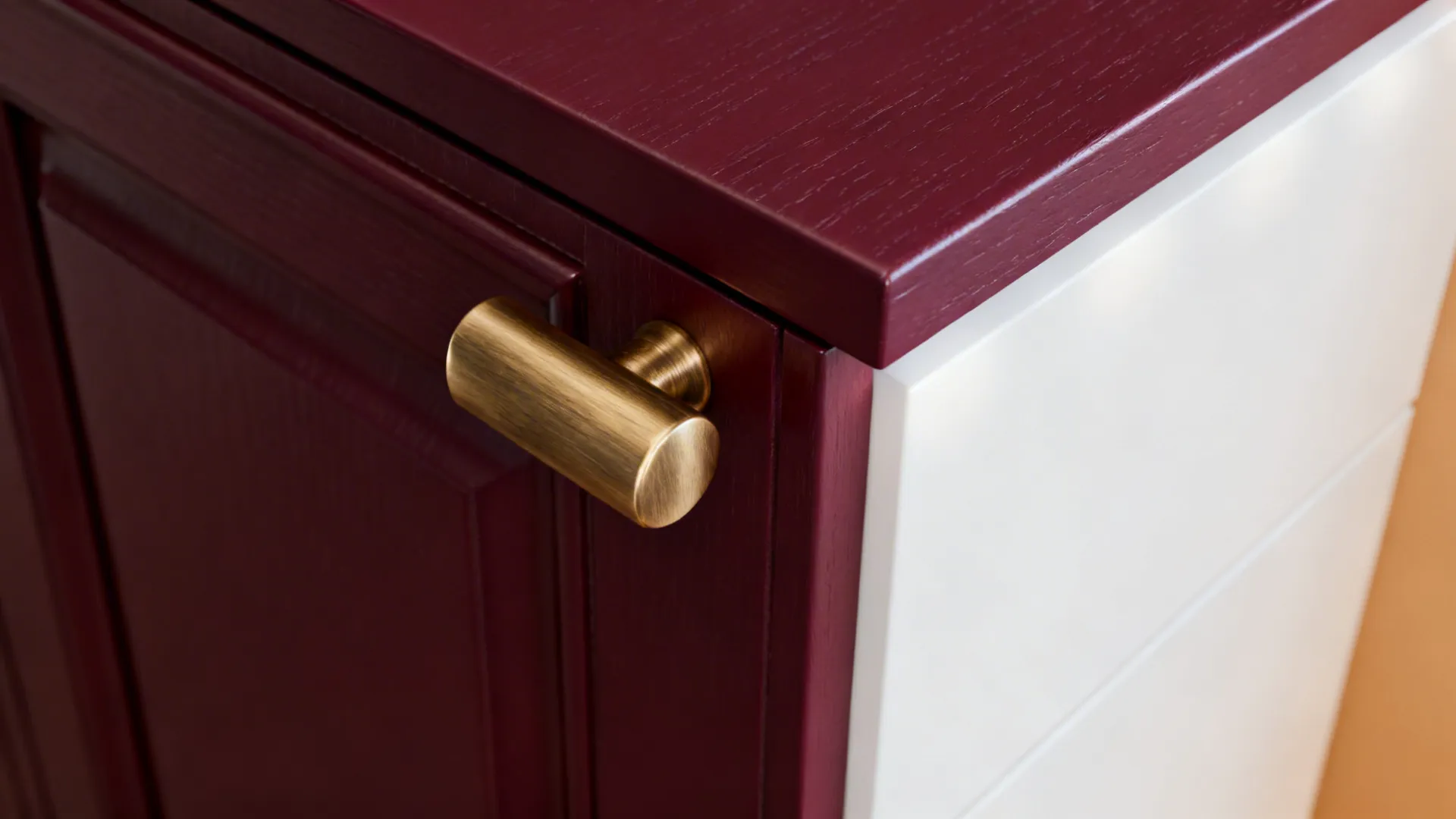 Macro of deep maroon cabinet with brushed brass pull and warm white nearby.