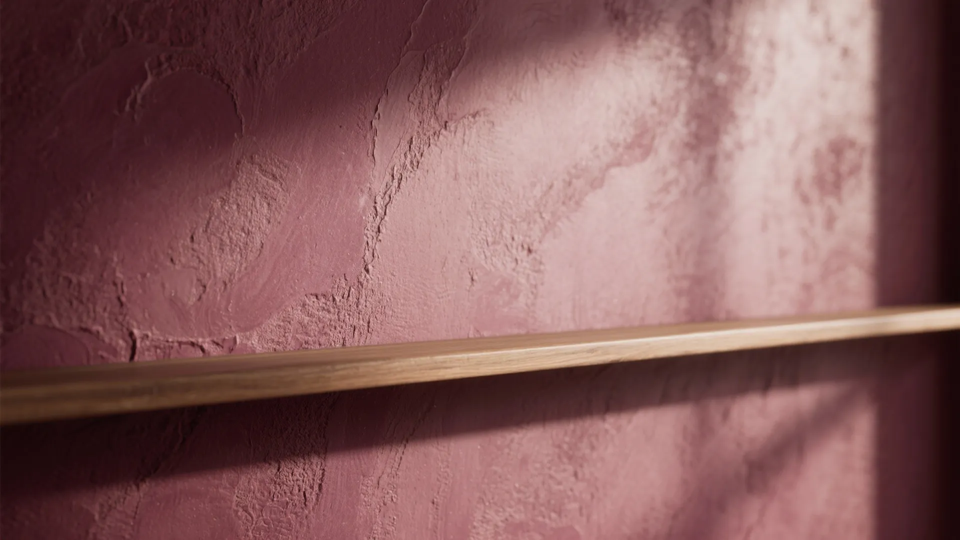 Close up view of a textured dark red wall with a simple wooden wall shelf
