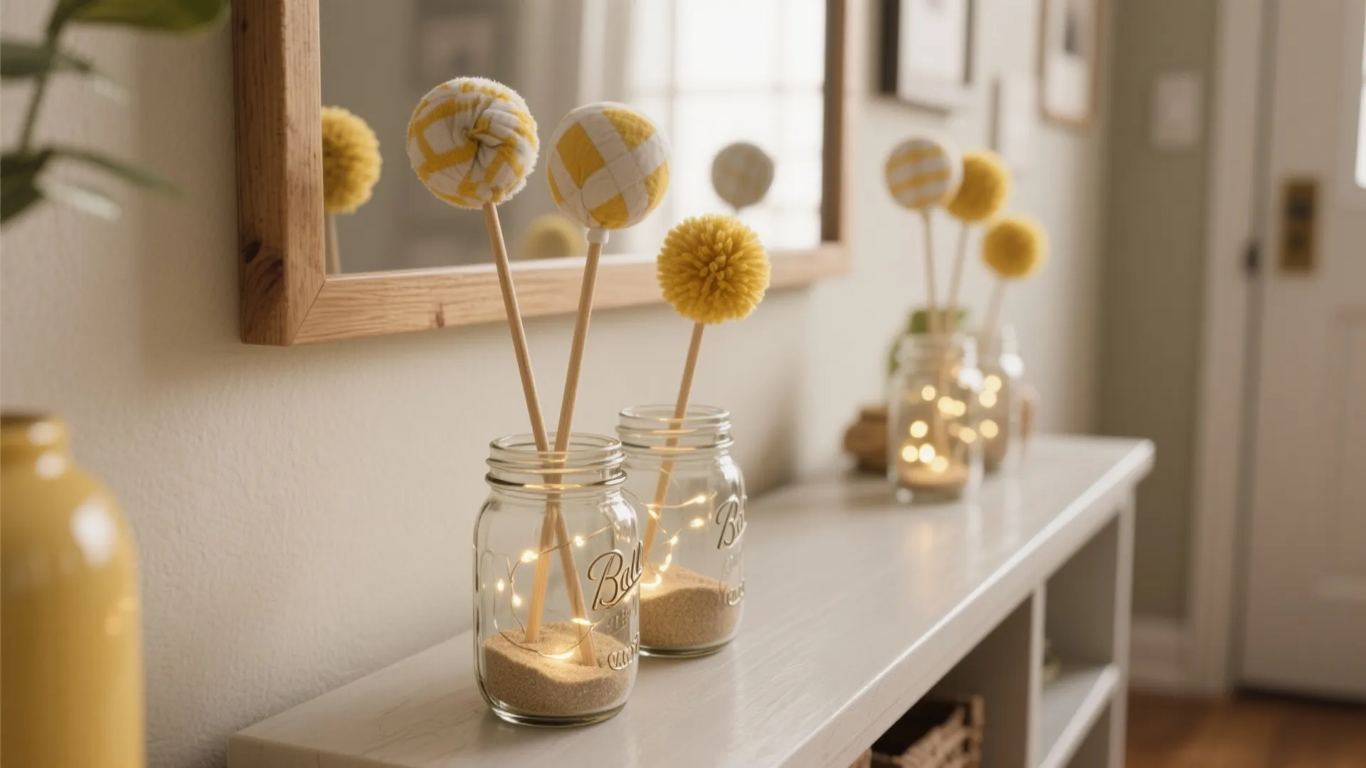 Glass jars with yellow pom-poms and small fairy lights placed on a white storage cabinet