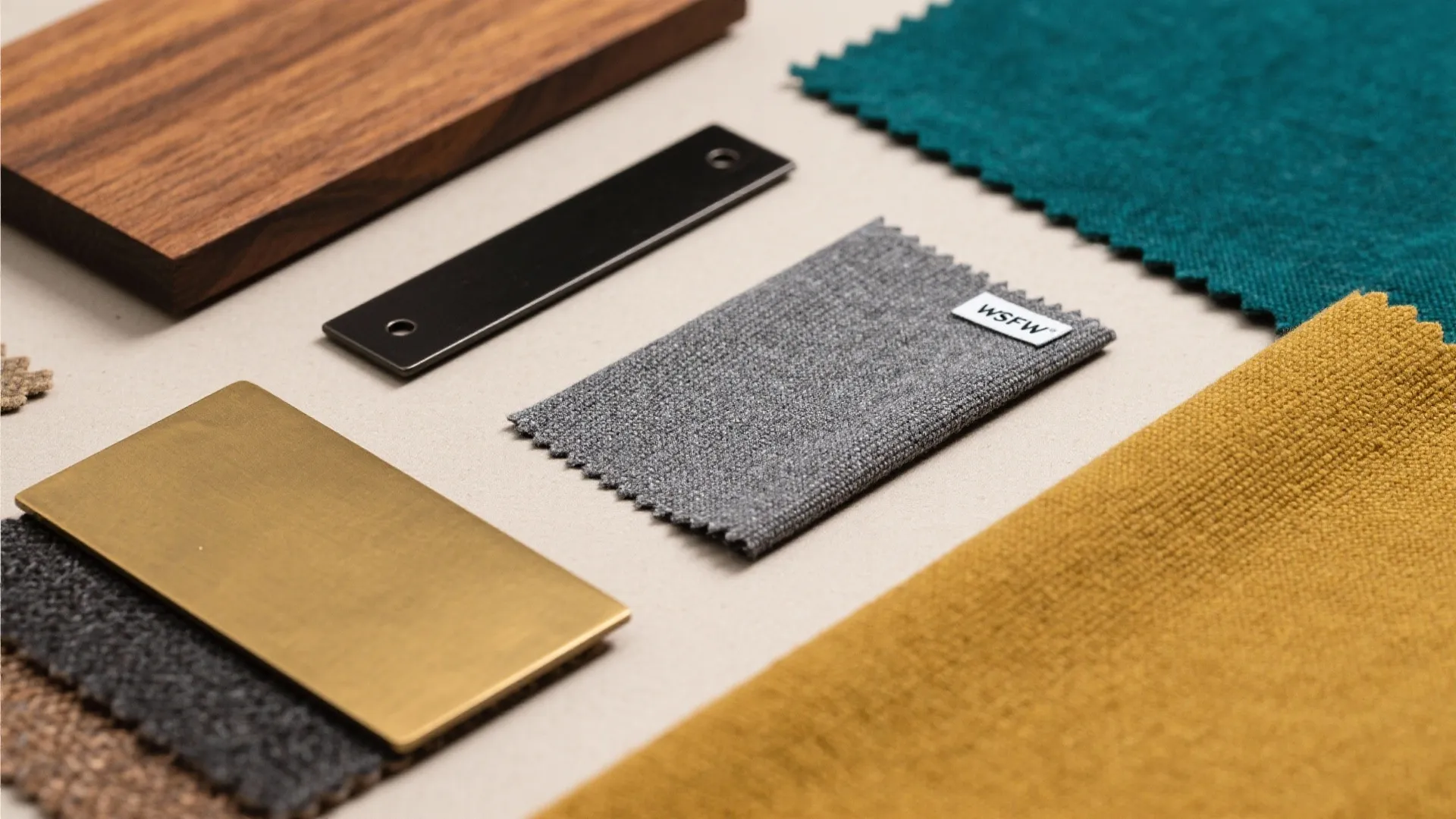 Interior design material samples including wood block metal plate and various colorful fabric swatches on table