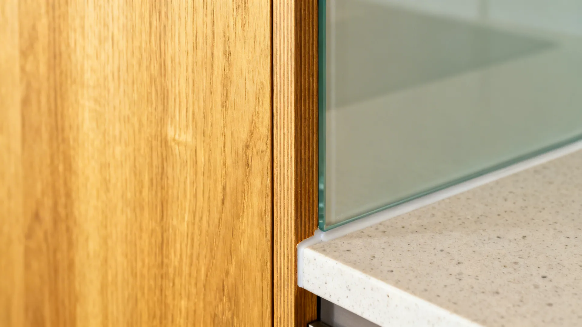 Close up view of wooden wall panel meeting a glass kitchen splashback and stone counter