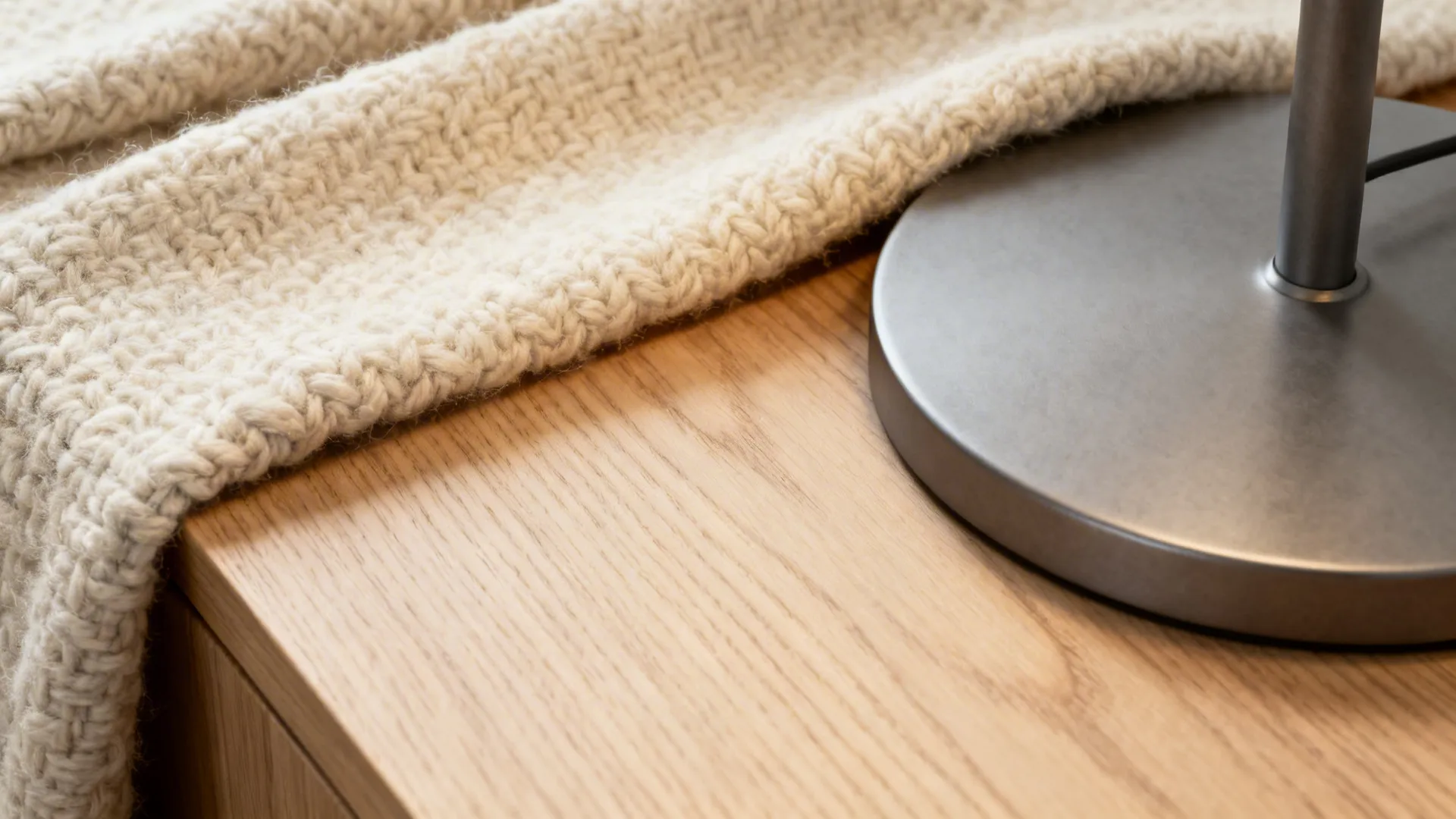 Macro view of wool throw, light oak grain, and matte metal base highlighting Scandinavian materials.