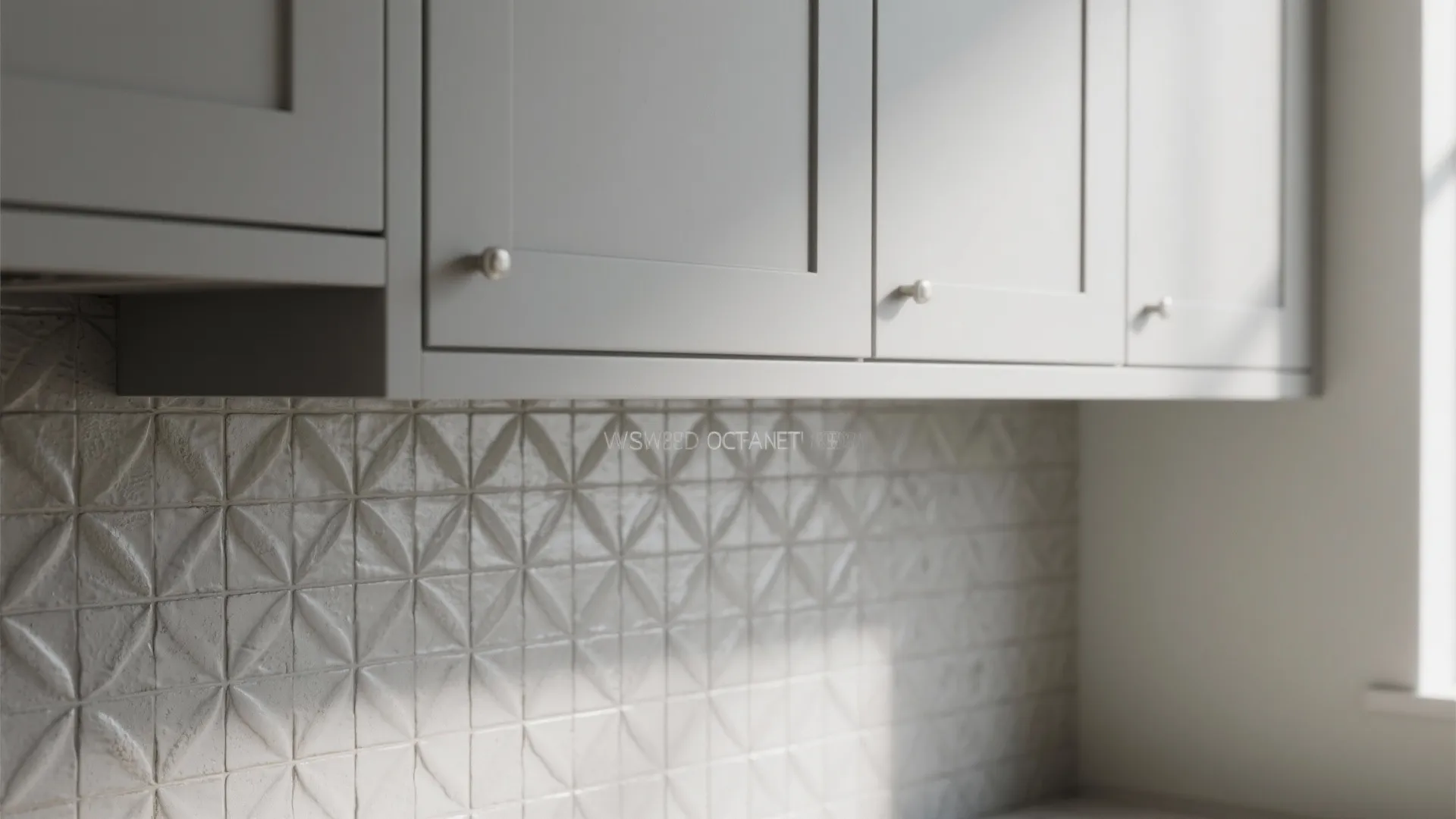 Close up of grey kitchen cabinets with small round handles above a textured white tile wall