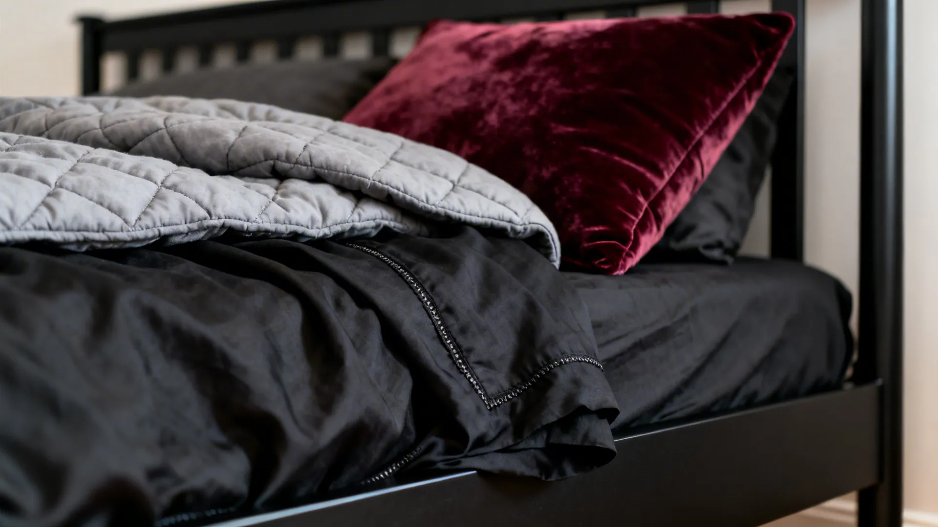 Close-up of matte black bedframe with charcoal bedding and burgundy cushion