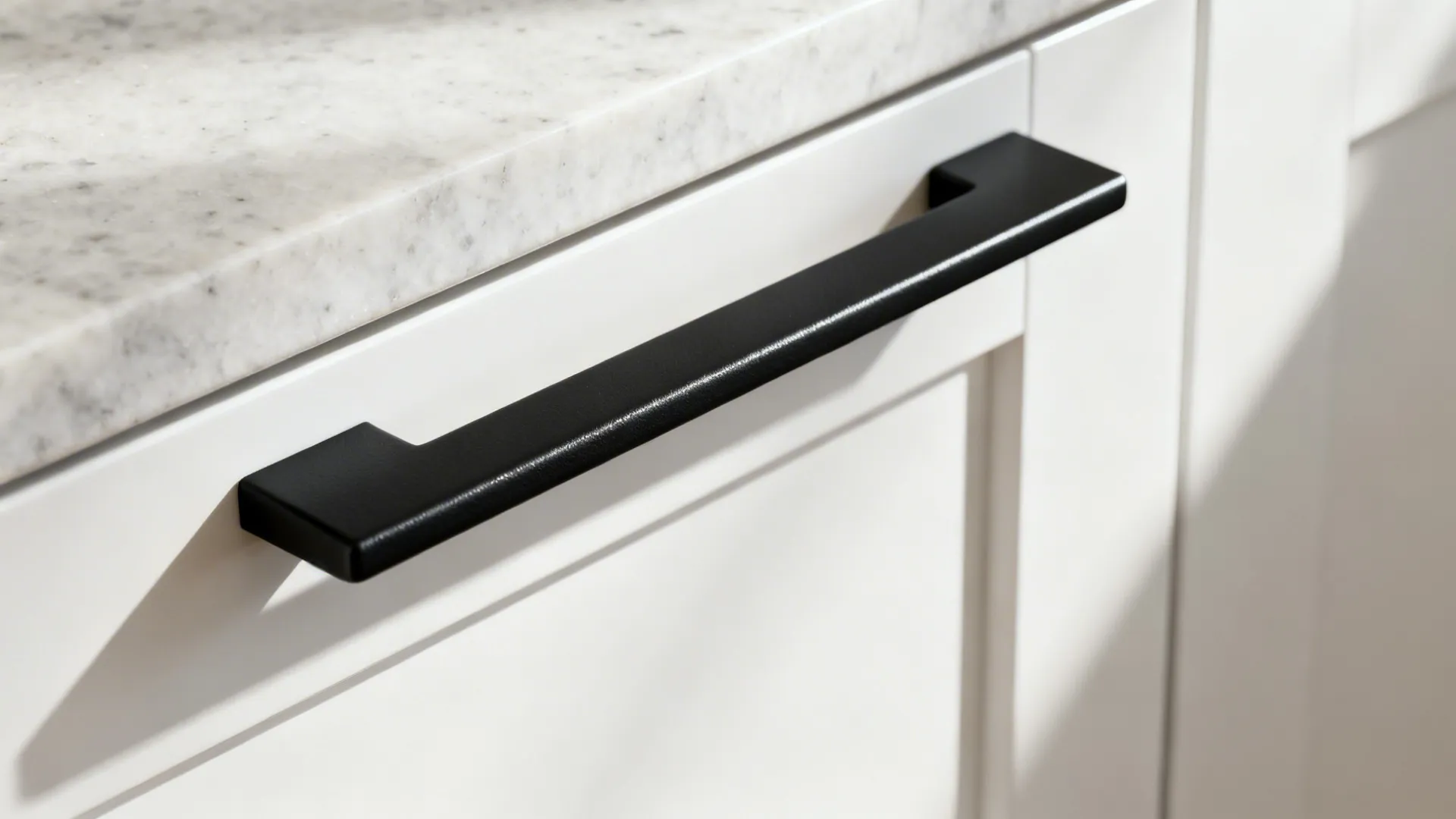 Macro view of a matte black bar pull on a white shaker cabinet showing fine texture.