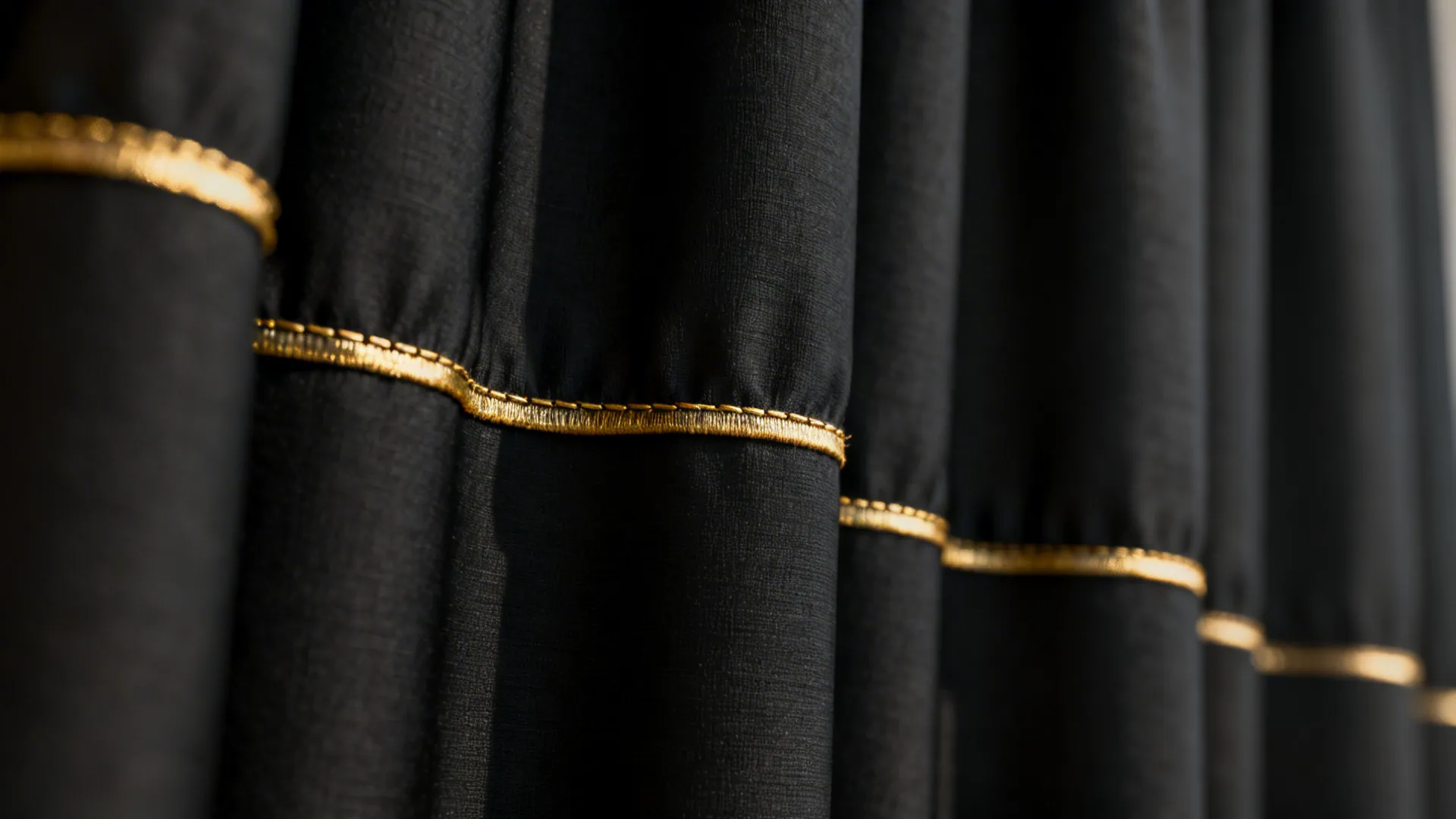 Close-up of black fabric curtain folds featuring a thin horizontal gold trim line for decoration