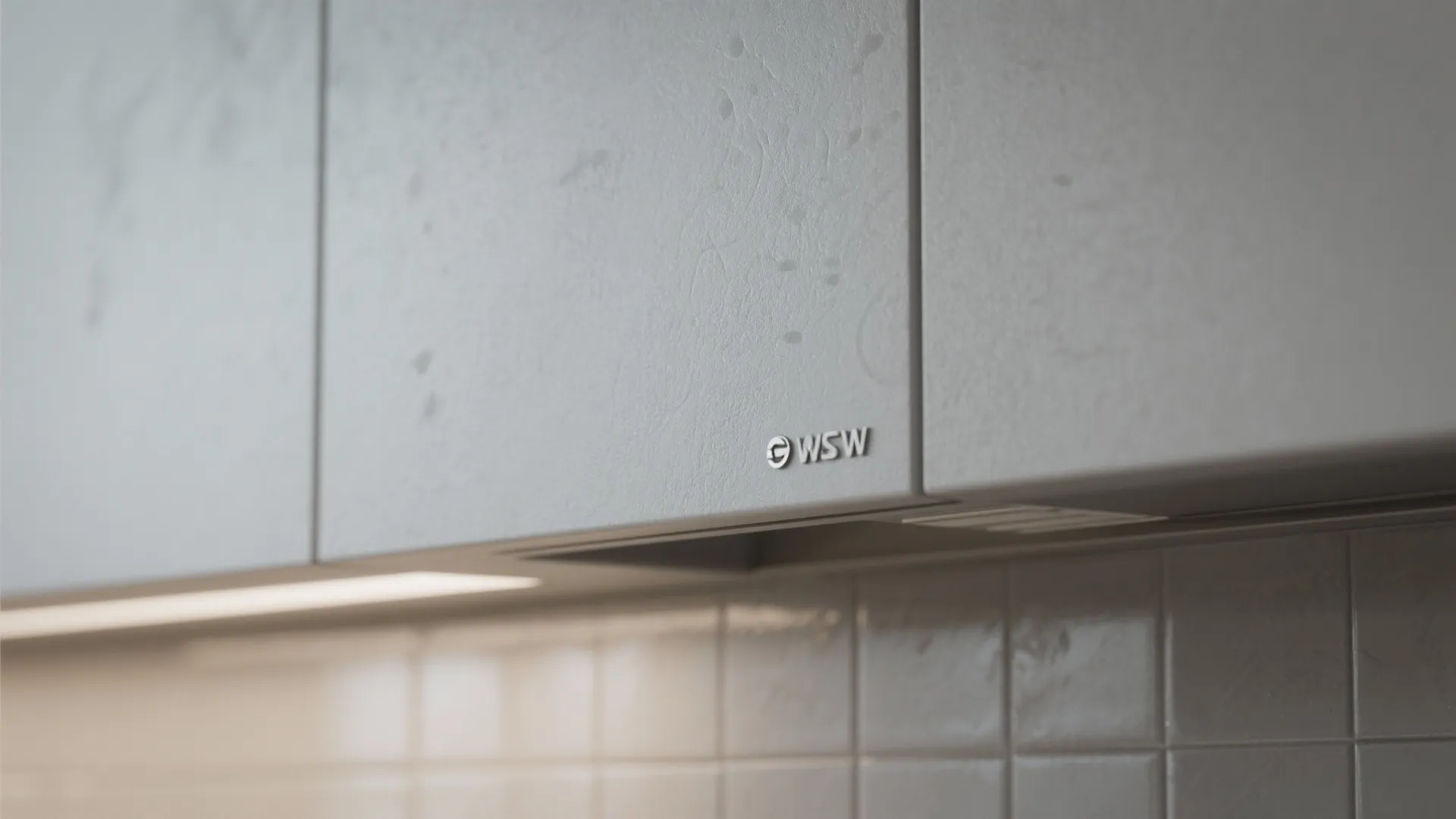 Close up of matte grey kitchen cabinet doors with small logo above white tiled wall