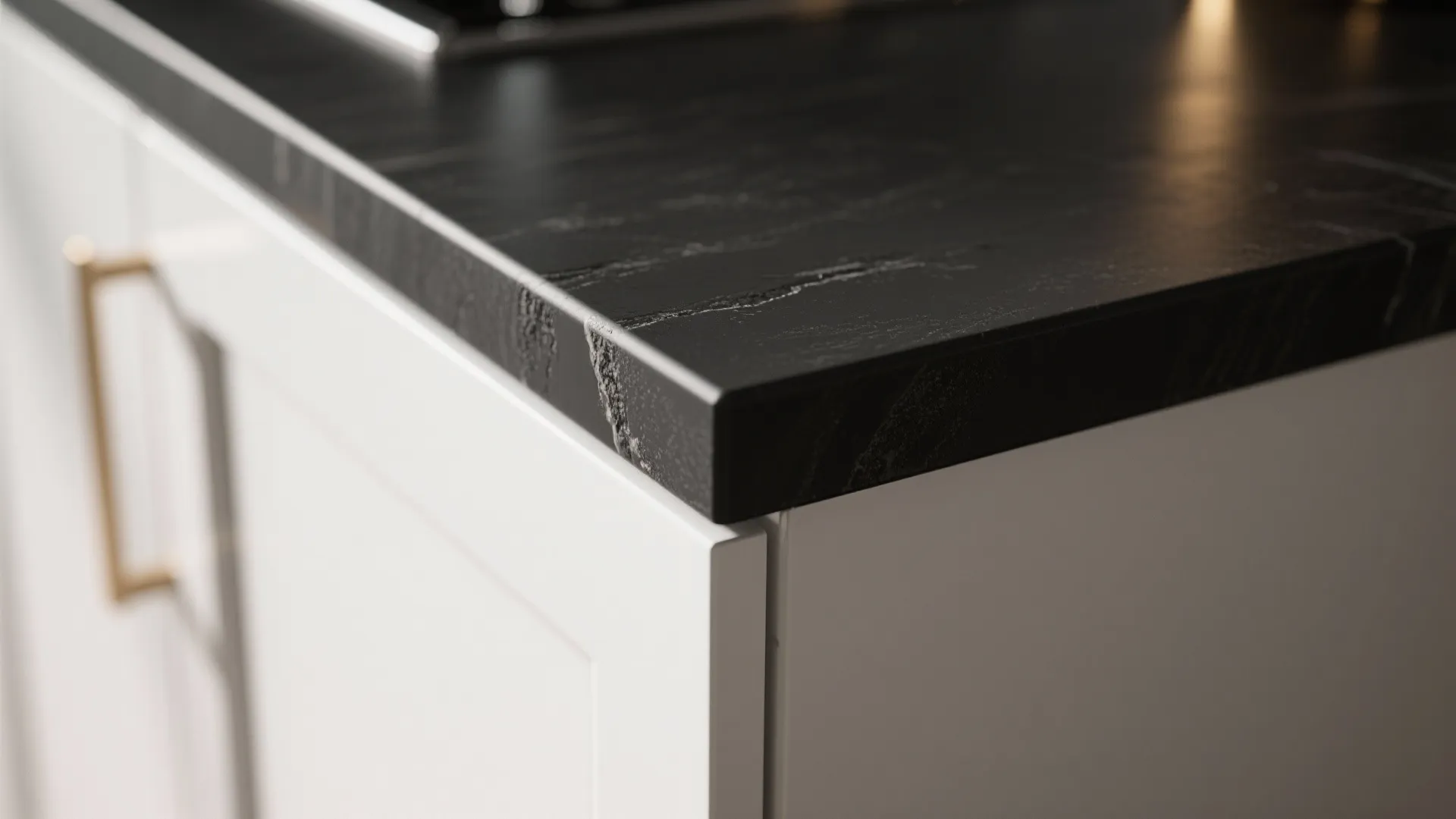 Macro view of a matte black countertop meeting satin white cabinet with eased edge.