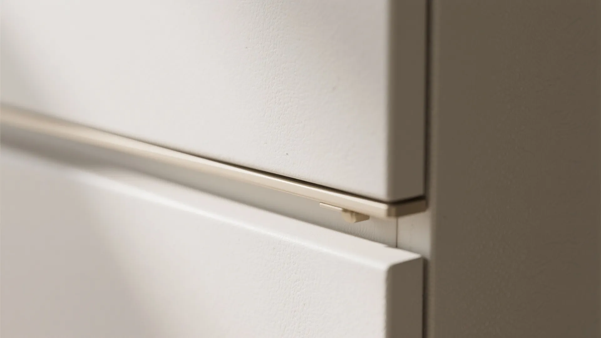 Close up of a white cabinet door with a slim metal handle and matte textured finish