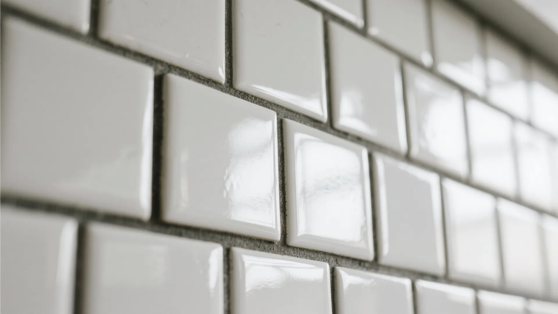 Close up view of white square tiles with grey grout and shiny surface on wall