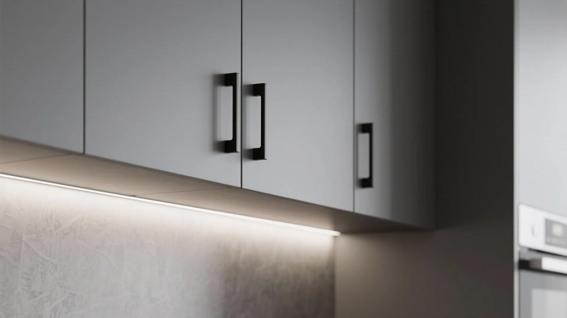 Close up of matte grey kitchen cabinet doors with black handles and under cabinet lighting