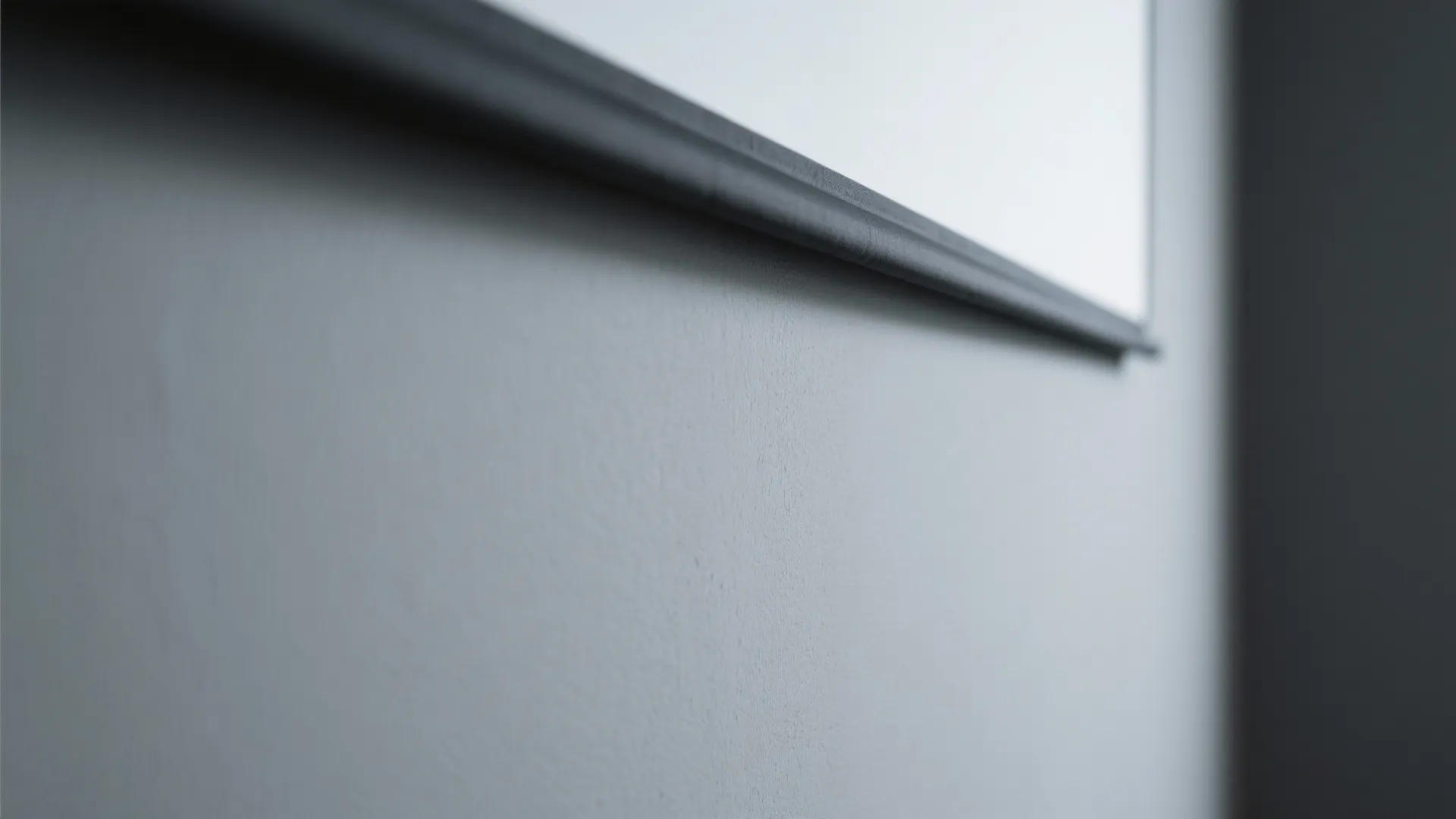 Macro of matte neutral gray wall behind a projector screen with smooth finish and soft light absorption.