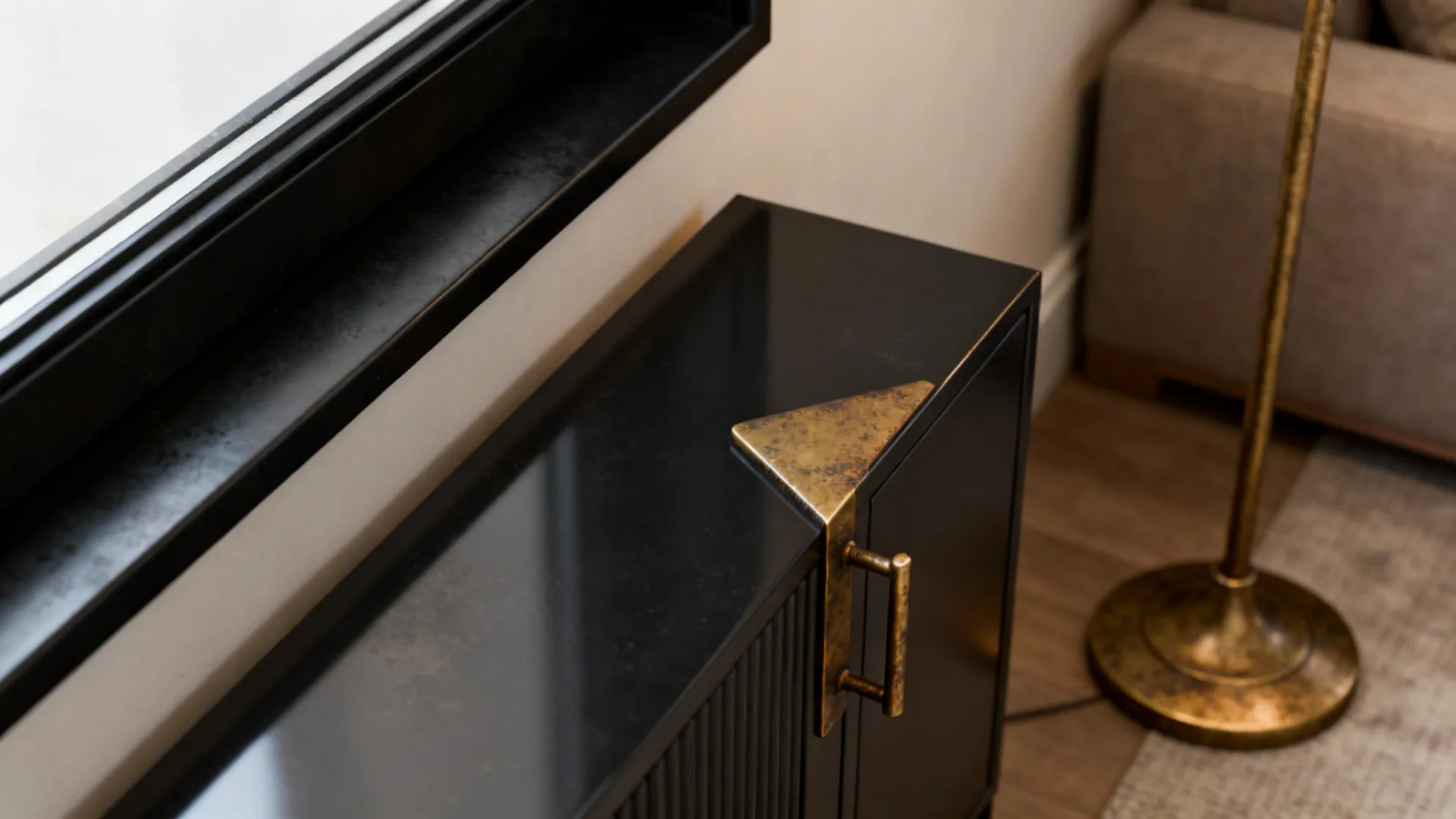 Matte black and aged brass fixtures including a lamp base and cabinet pull in a farmhouse living room.