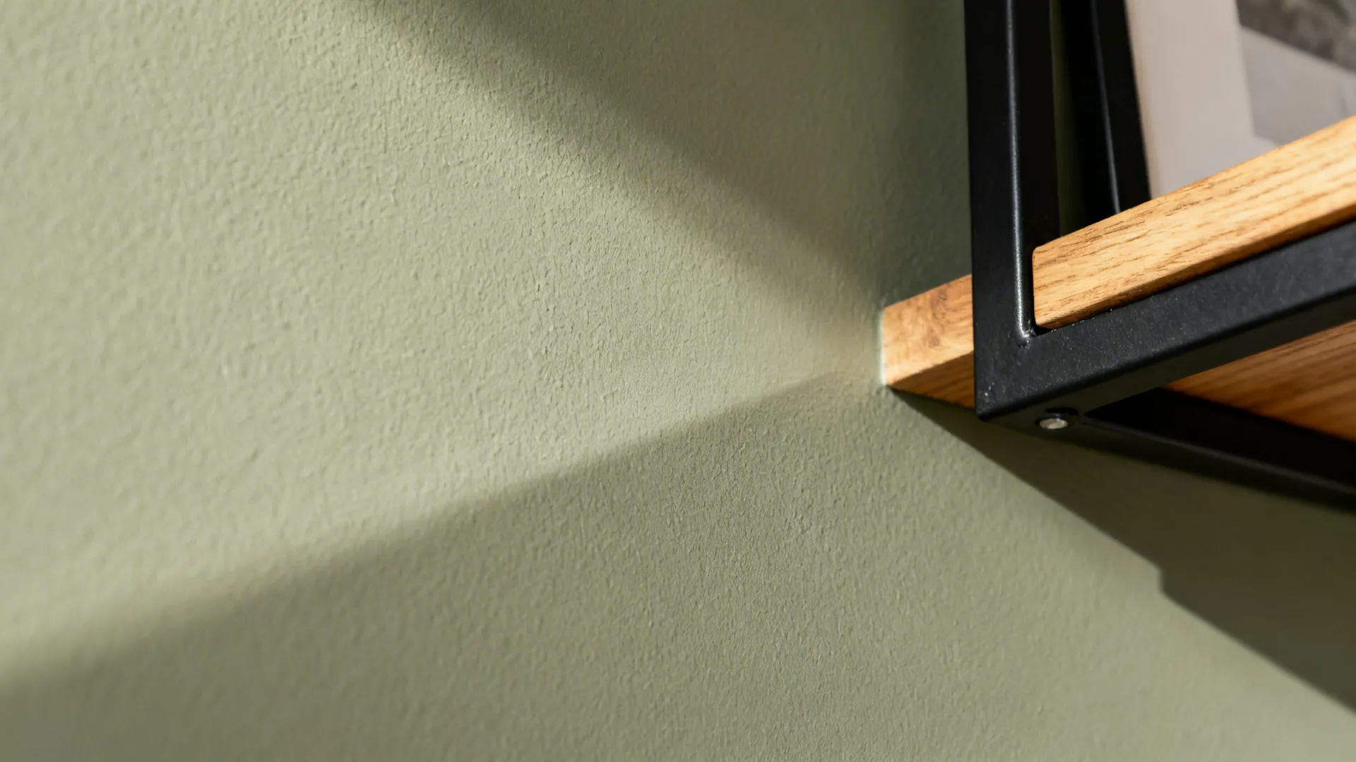 Close up of a green textured wall with a wooden shelf and black metal frame