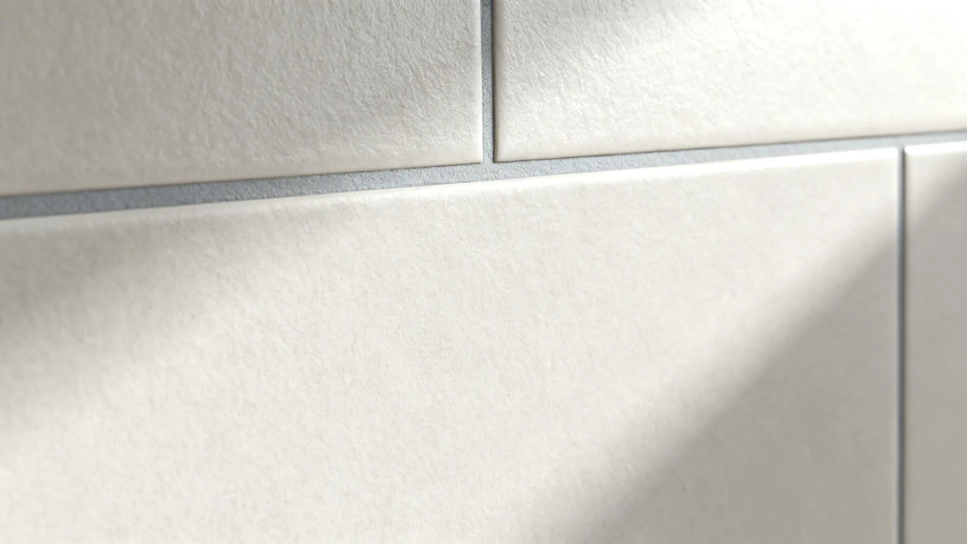Close up view of matte white wall tiles with grey grout lines and soft morning sunlight