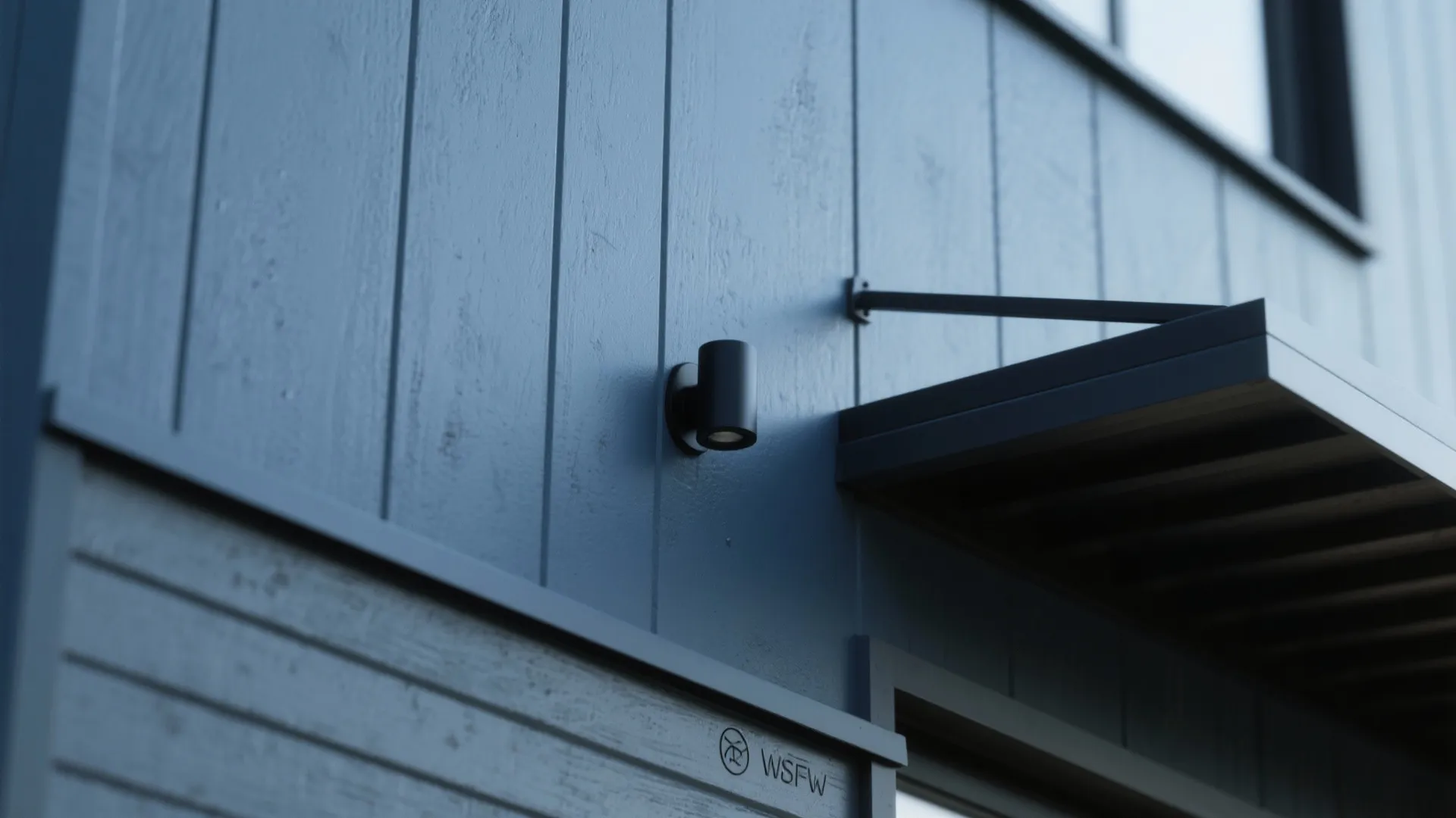 Modern blue wall panel exterior with black wall light fixture and dark metal porch roof
