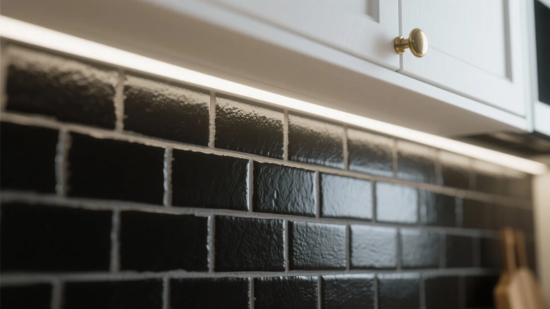 Macro view of matte black subway tile backsplash with soft under-cabinet lighting and brass hardware edge.