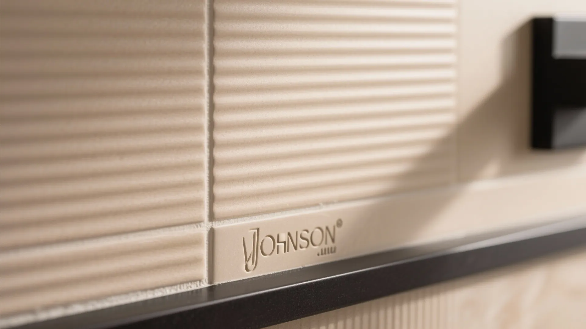 Close up of beige wall tiles with horizontal lines showing brand name and soft light shadow