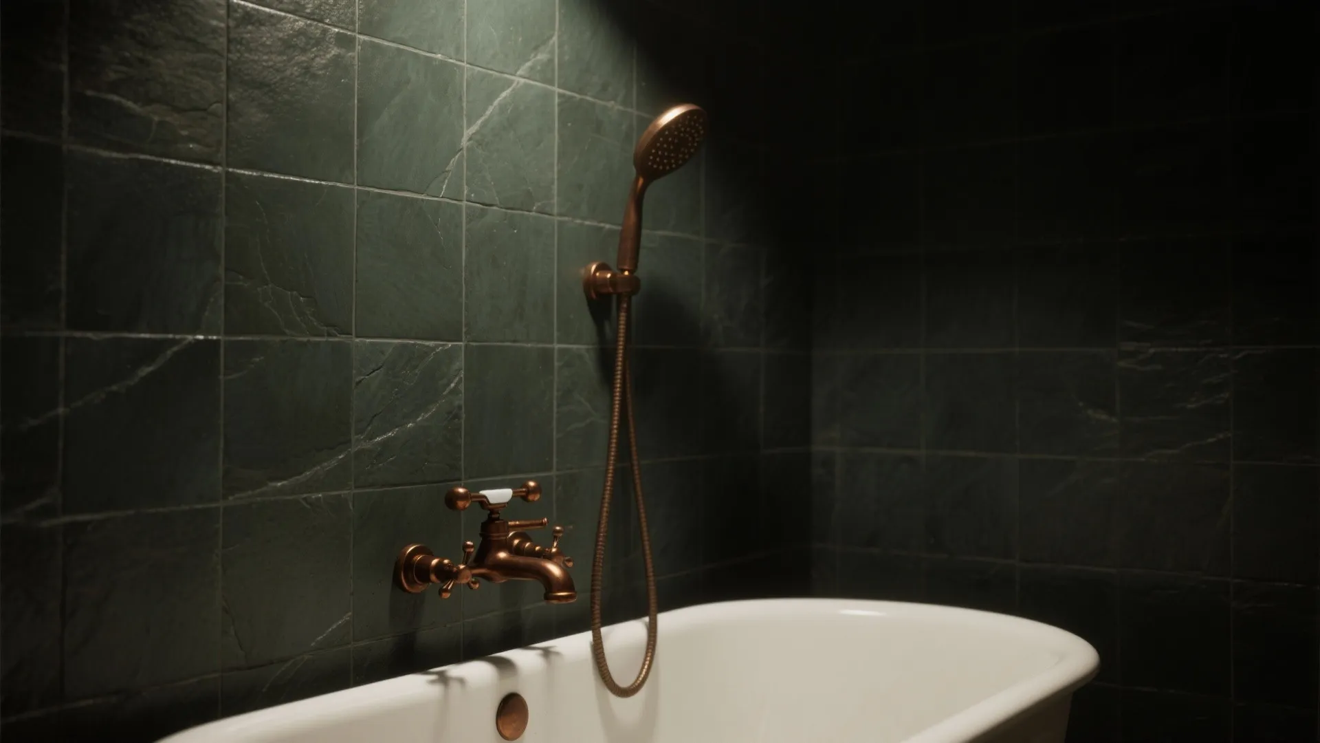 White bathtub with bronze faucet and shower head against dark green textured stone bathroom wall tiles