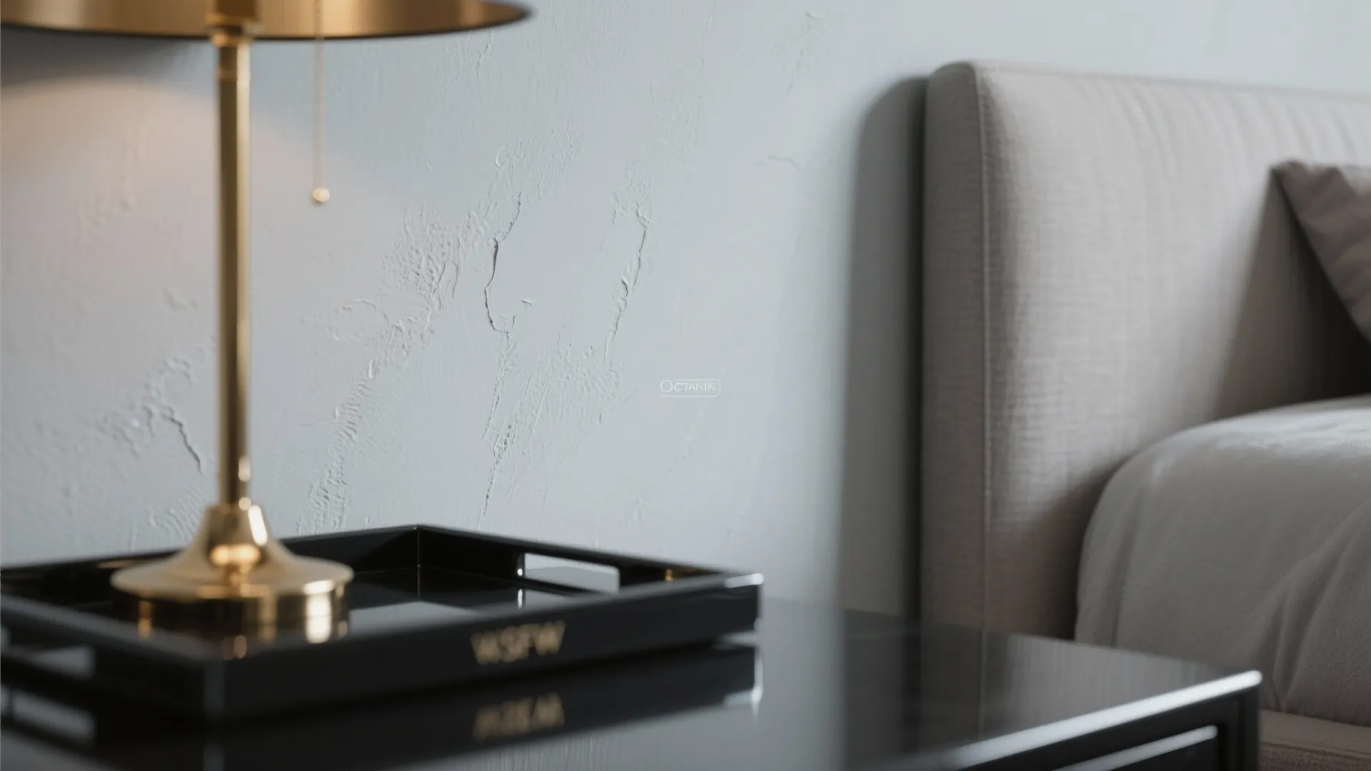 Close up of bedroom showing textured white wall with gold table lamp on black tray