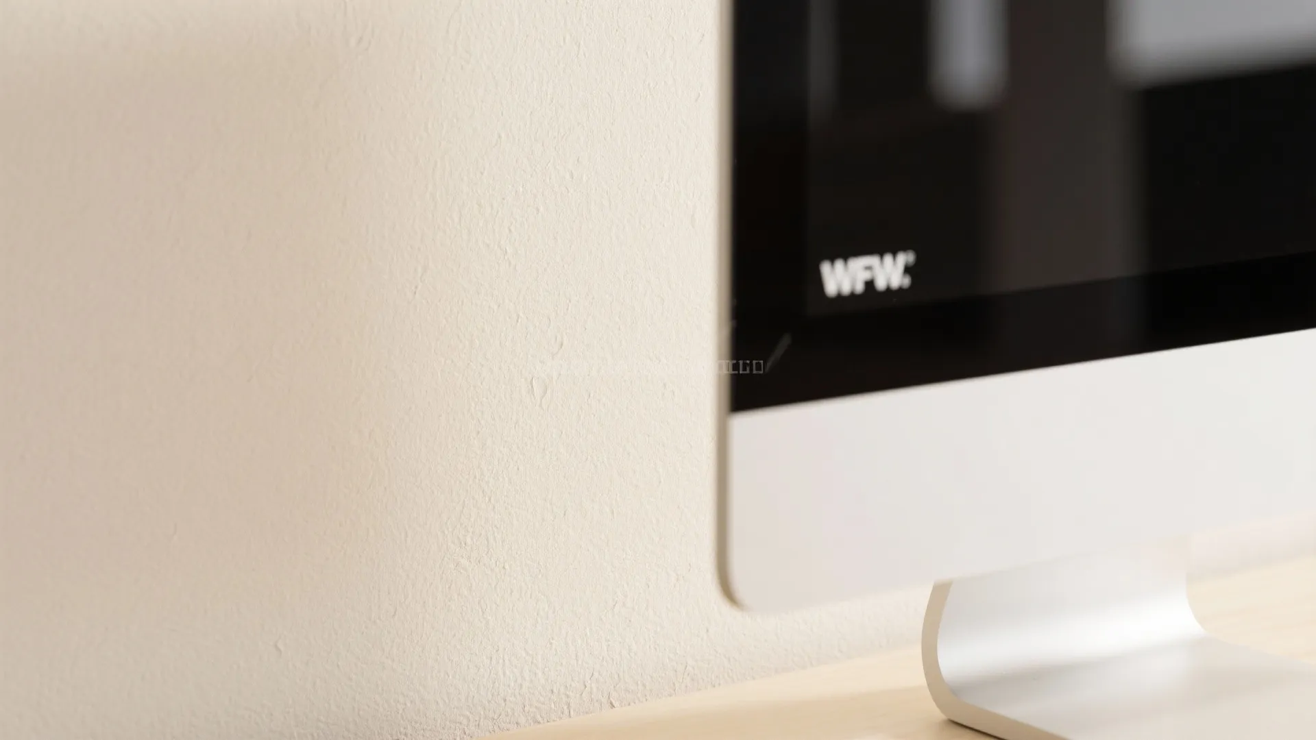 Close up of a computer monitor on a wooden desk against a plain beige wall