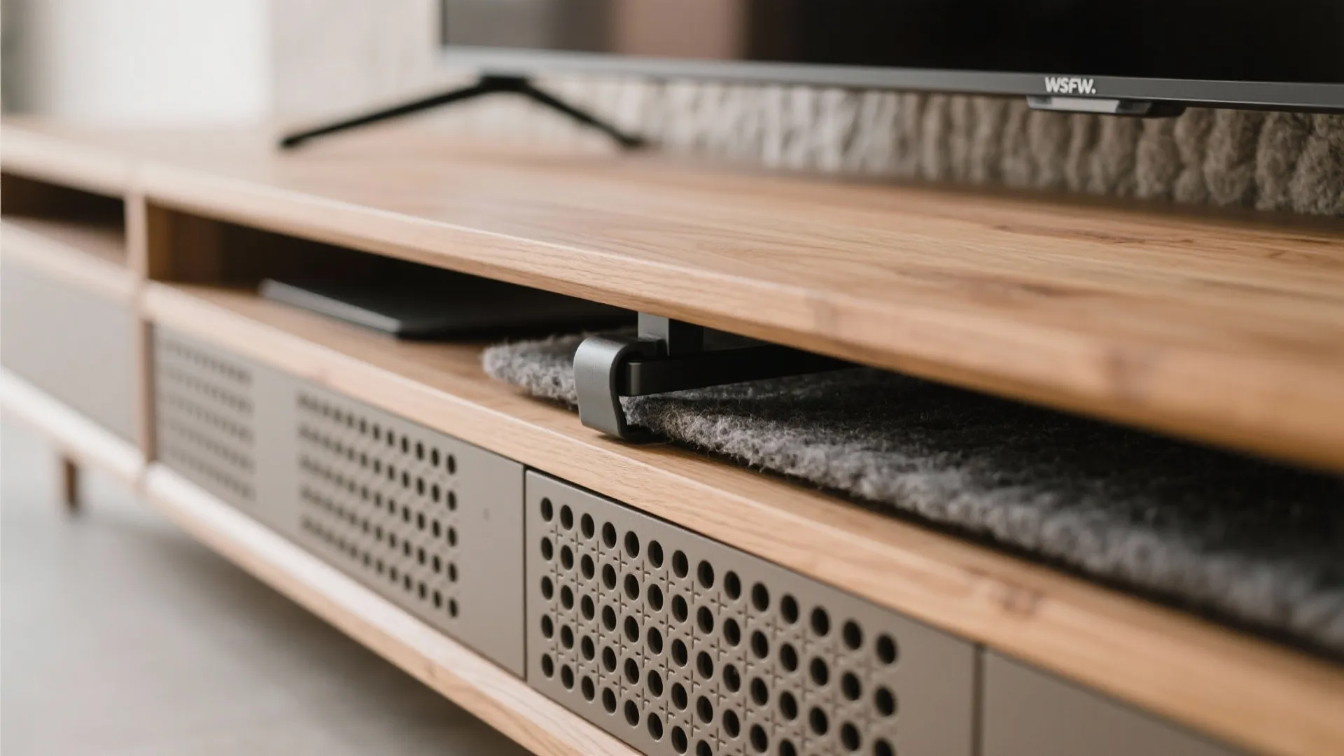 Close-up of soft-close hinge, perforated grille, and ventilation gap on a media bench with felt wall.