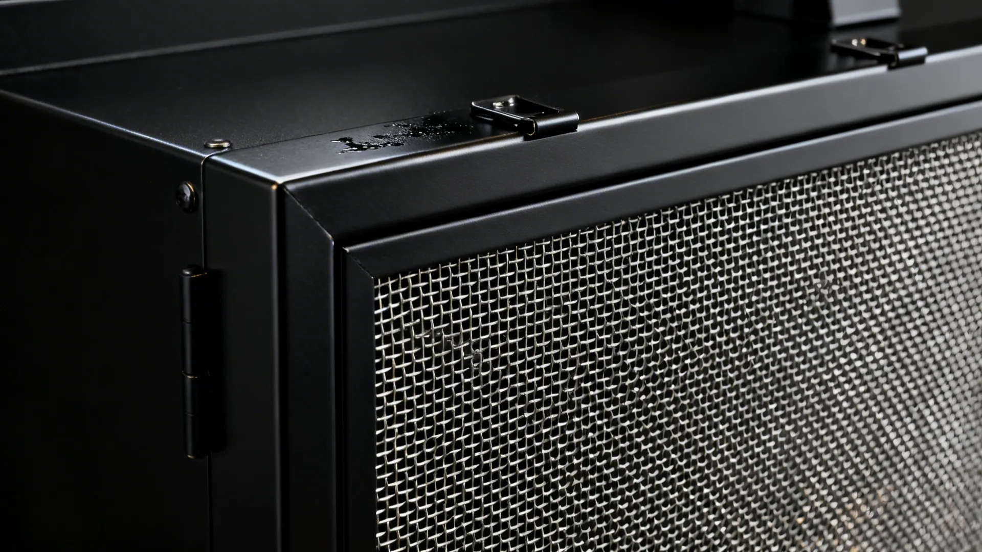 Close-up of a removable stainless mesh clipped into a satin black aluminium frame above a hob.