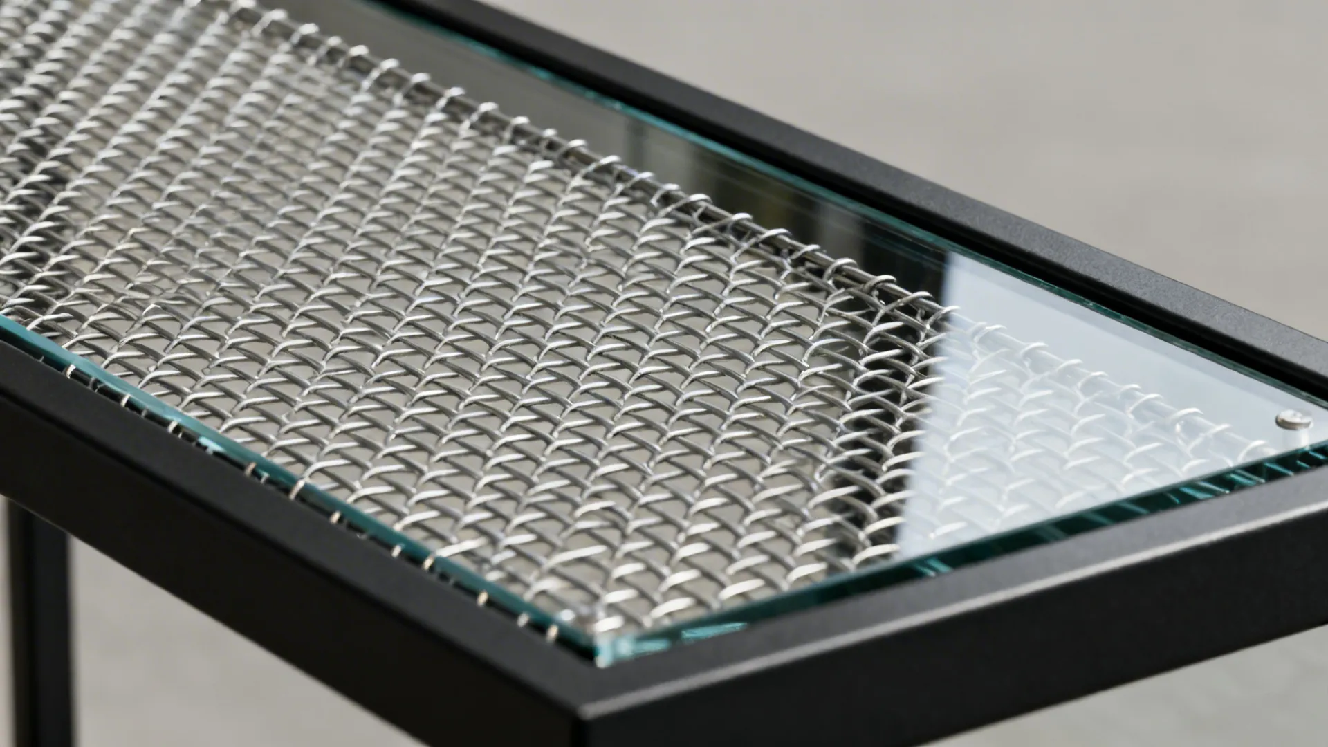 Macro detail of woven steel mesh layered behind tempered glass.