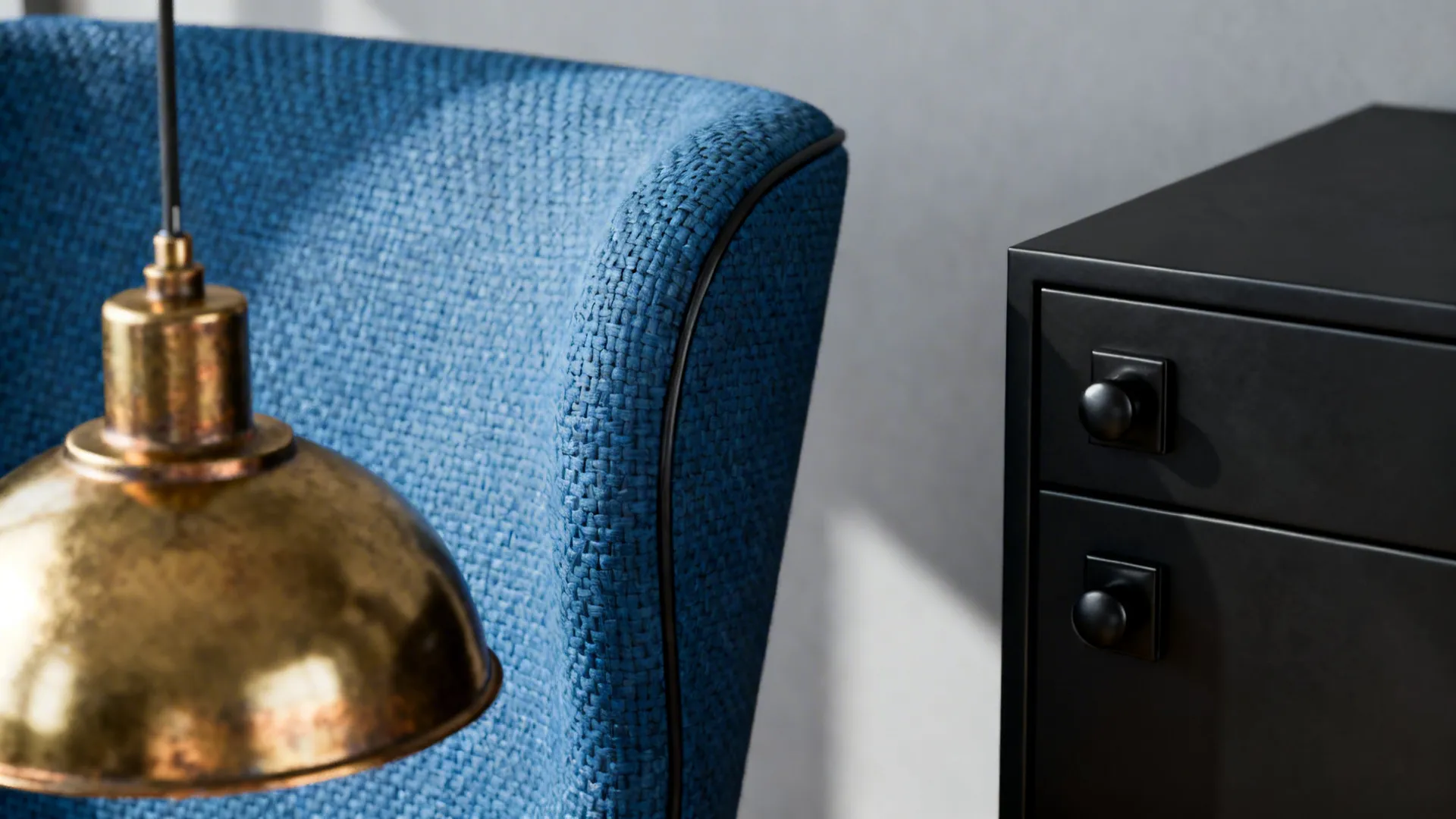Close-up of blue chair upholstery beside brass and matte black metal finishes