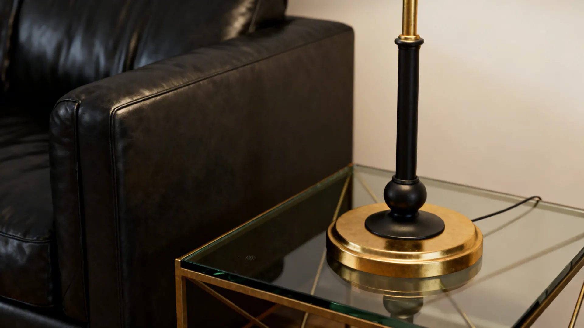 Brass lamp and glass-top table anchoring a black leather sofa