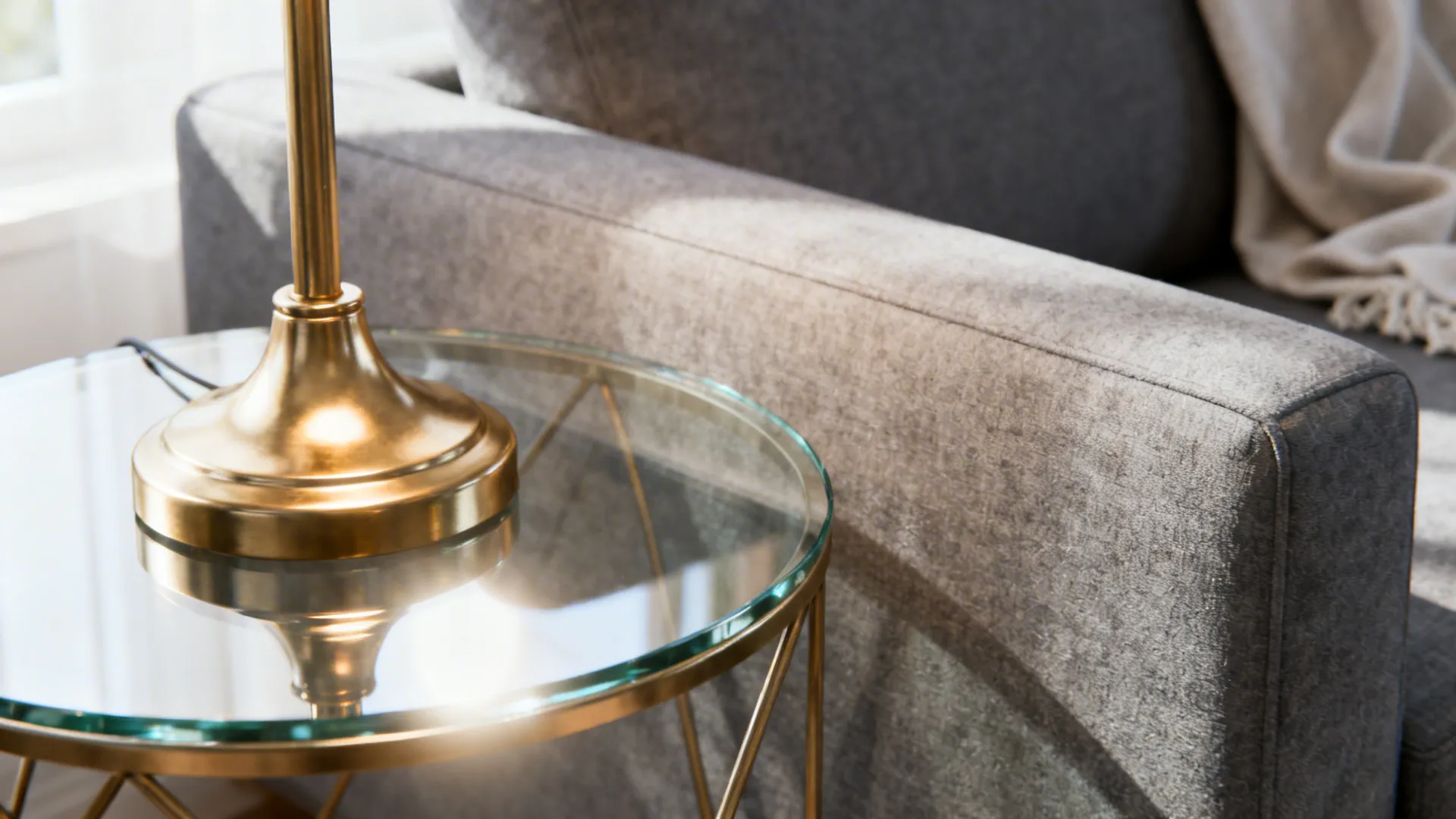 Brass lamp and glass table reflecting light to lighten a grey-heavy room.