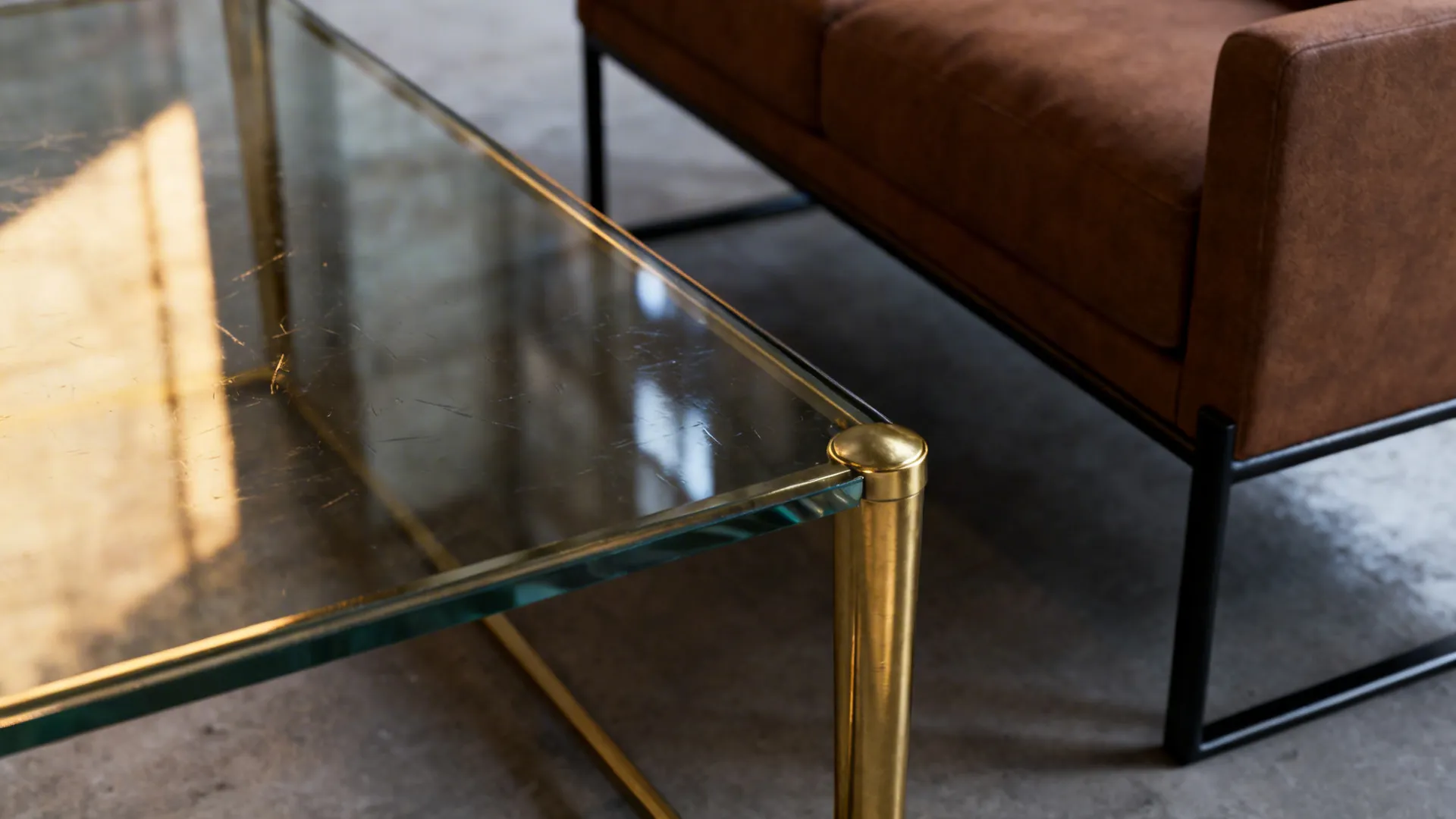 Close up of a glass coffee table with gold metal legs and a brown leather sofa