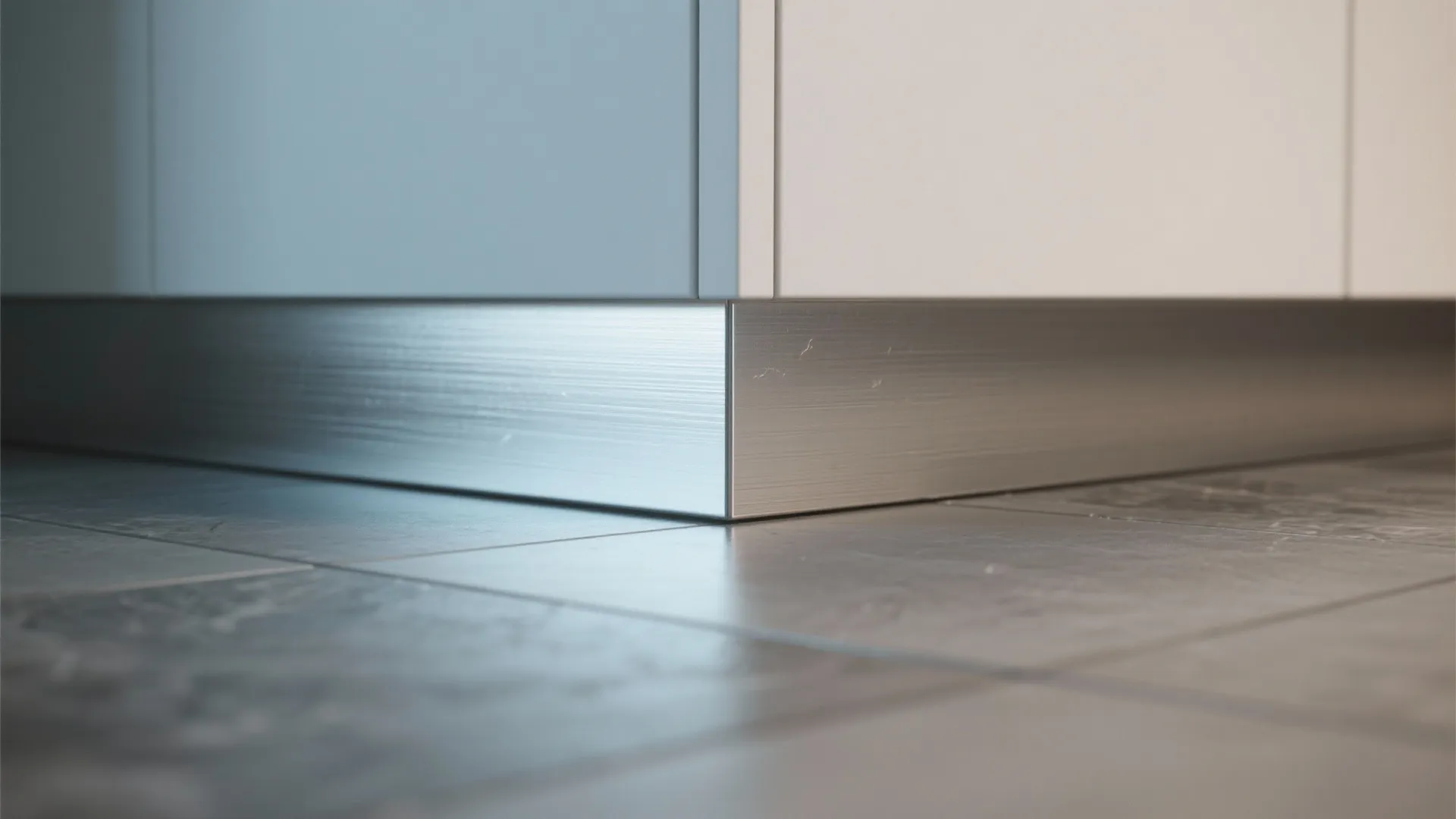 Modern brushed metal base under white kitchen cabinets installed on a dark grey stone floor