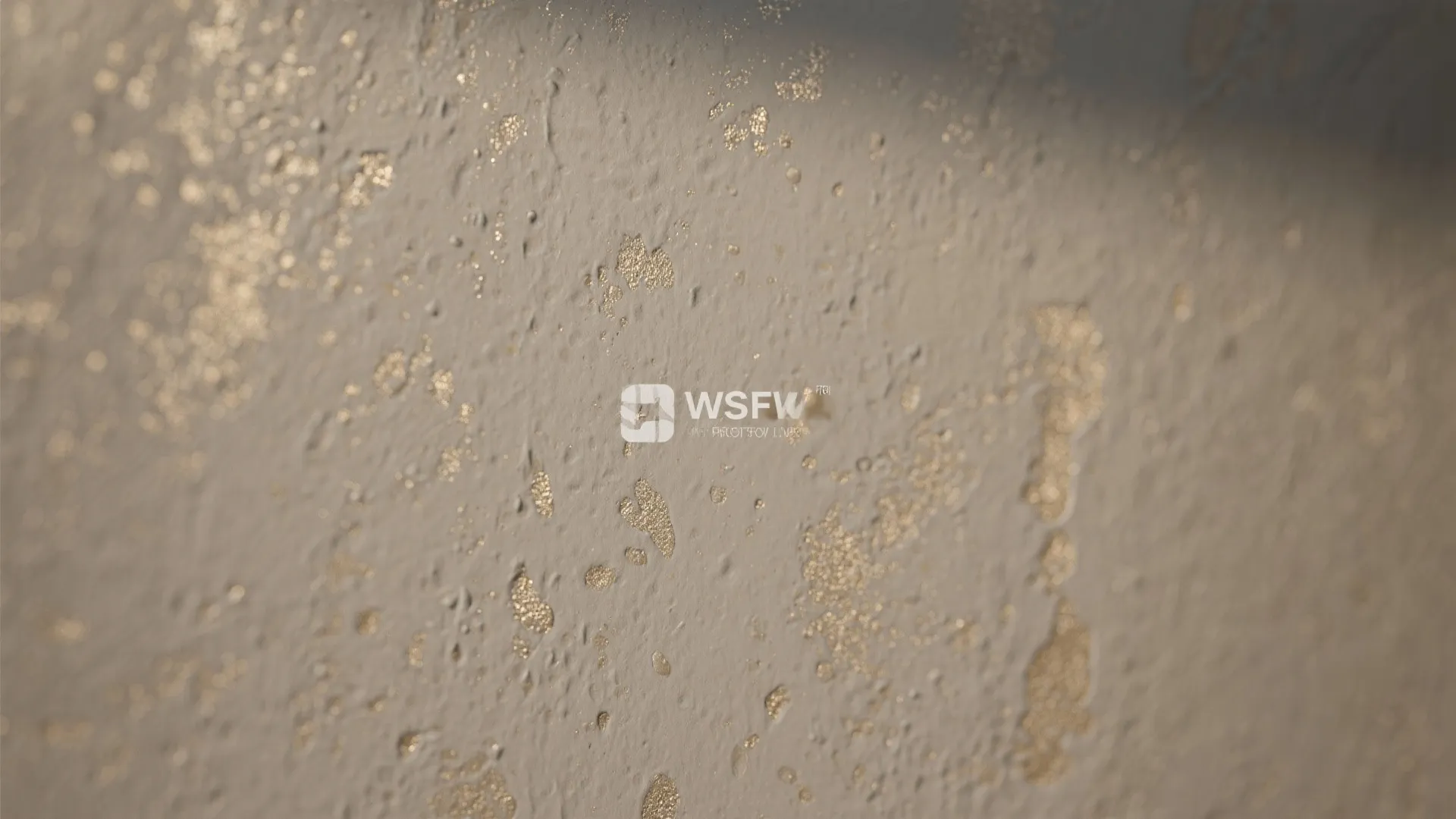 Close up of a beige textured wall featuring shiny gold metallic speckles and light shadows