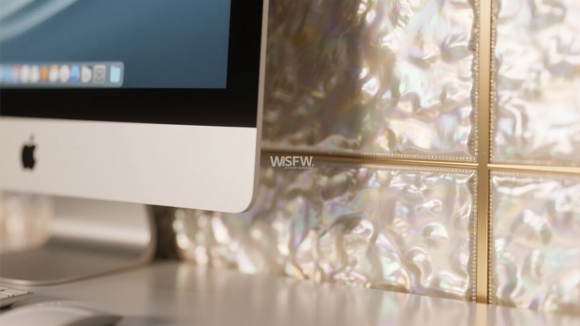 Macro view of a narrow pearlescent metallic wallpaper panel reflecting soft light behind a monitor.