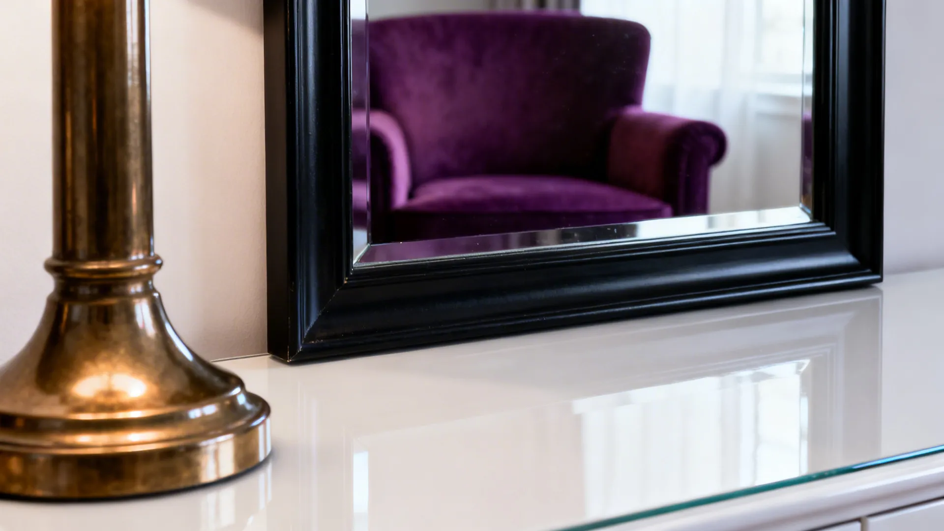 Brass lamp and black-framed mirror reflecting a plum armchair with a glossy white coffee table