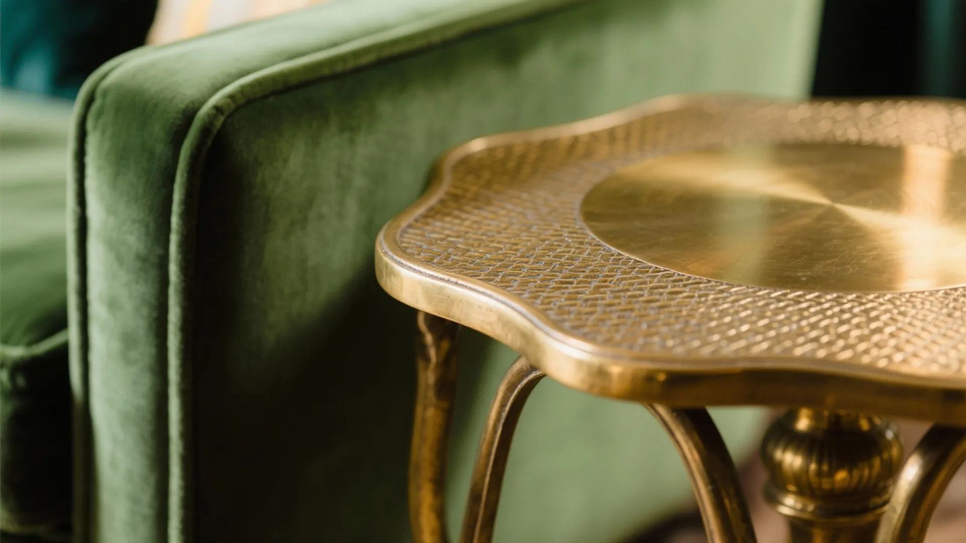 Gold metal side table with textured top placed next to a soft green velvet sofa