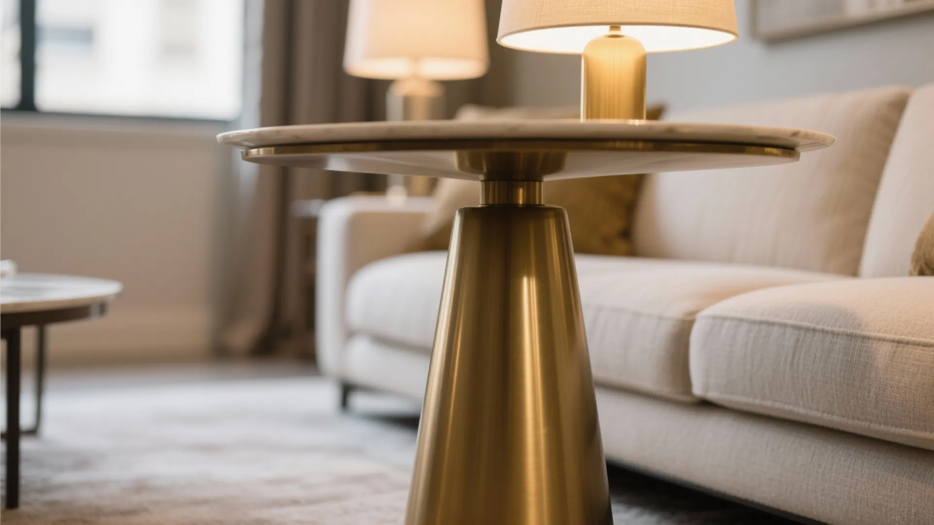 Gold side table with marble top next to beige sofa with a small table lamp