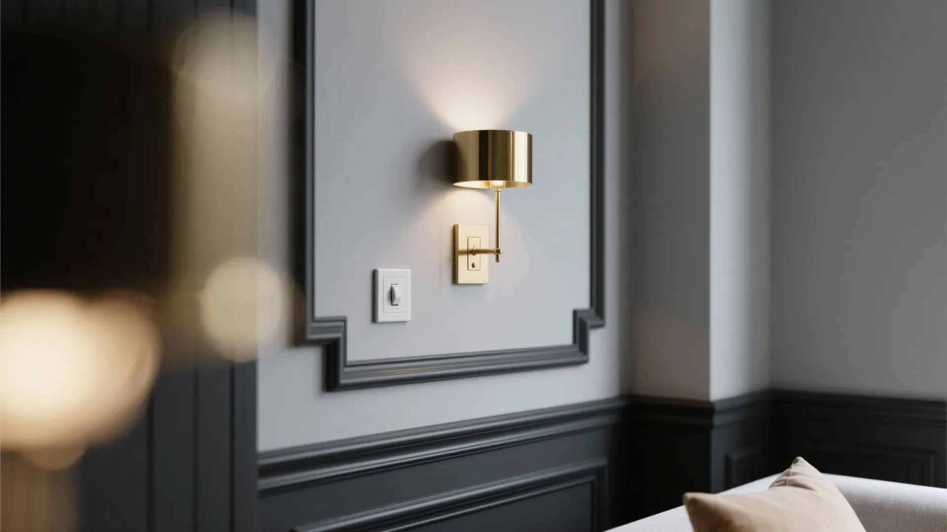 Modern gold wall light mounted on a grey wall panel next to a white light switch