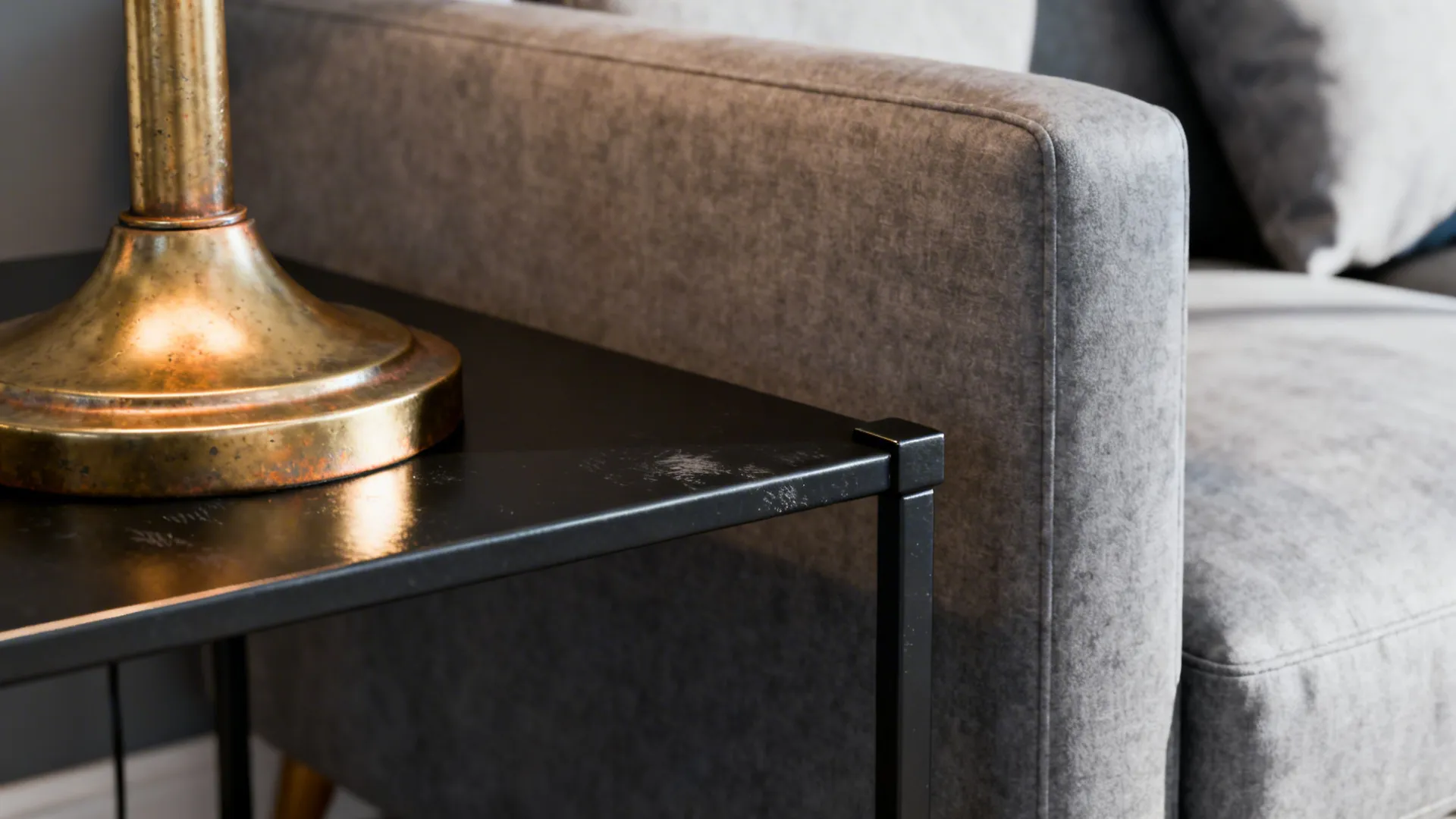 Gold lamp base on a black metal side table next to a grey fabric sofa