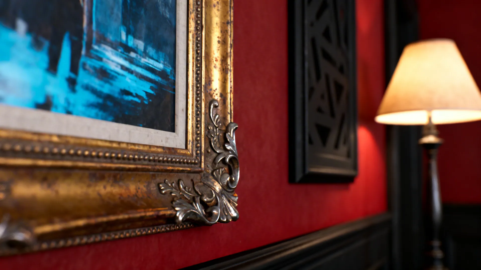 Brass lamp and gold frame with cooler-toned artwork on a red wall