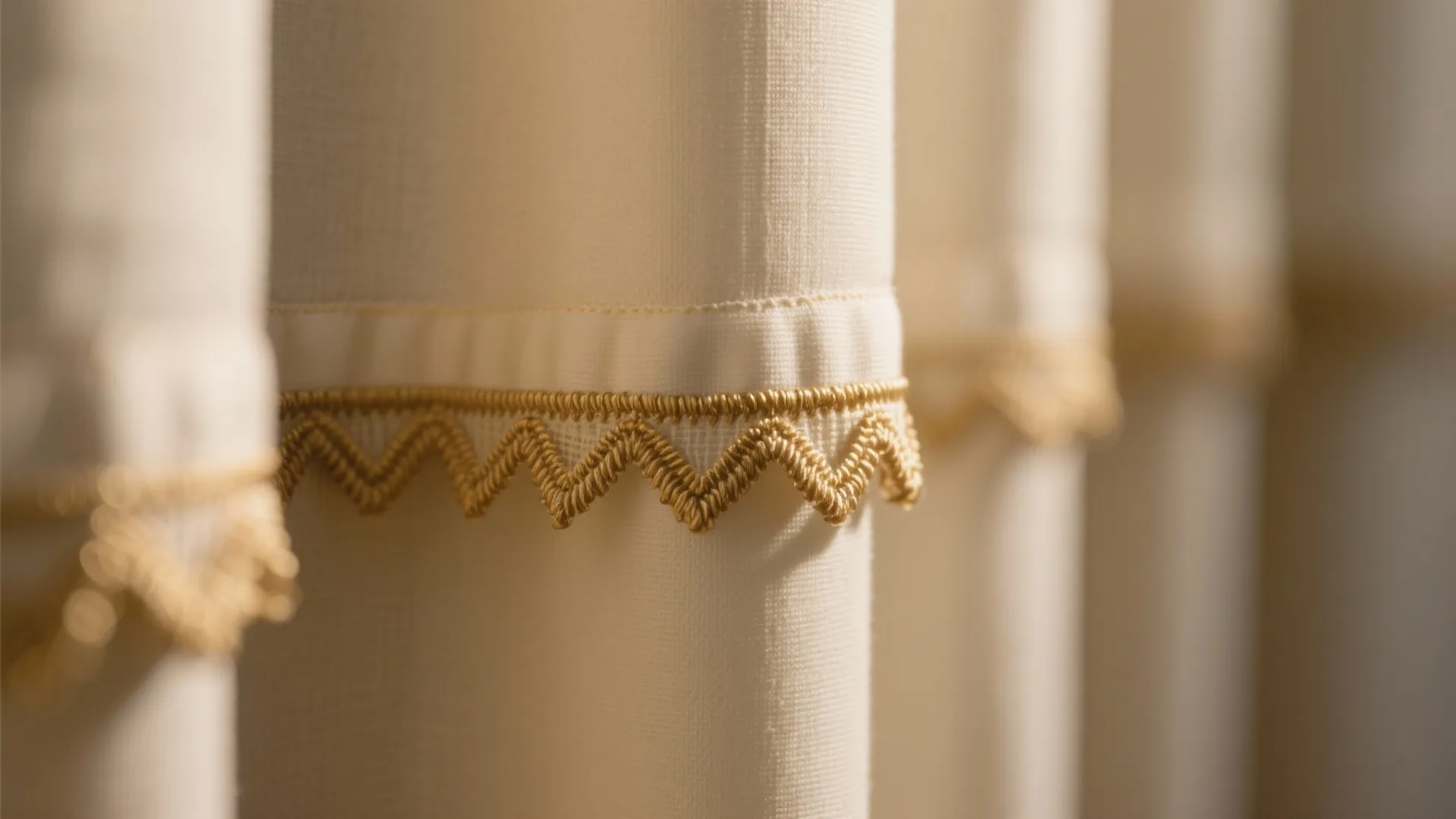 Close up of cream window curtains featuring a gold wavy decorative trim along the bottom