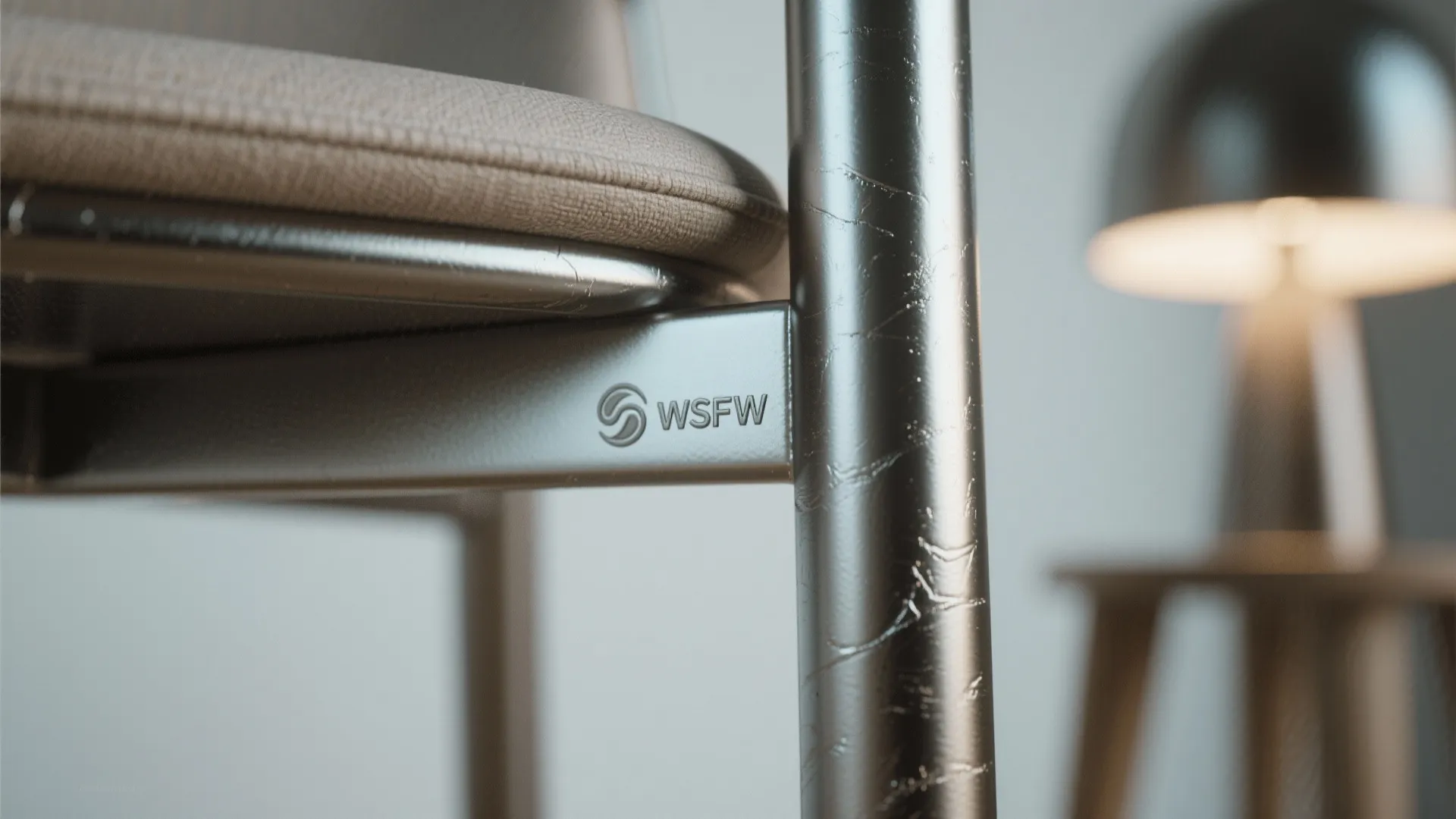 Close-up of metallic chair frame with logo beside a blurred round light fixture and table