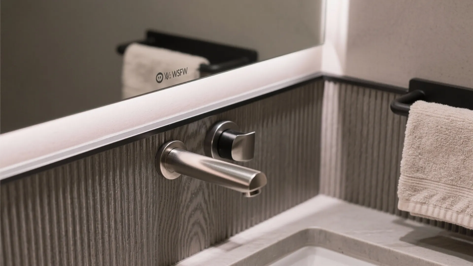 Modern bathroom detail featuring a silver wall mounted tap with textured grey wall panel background