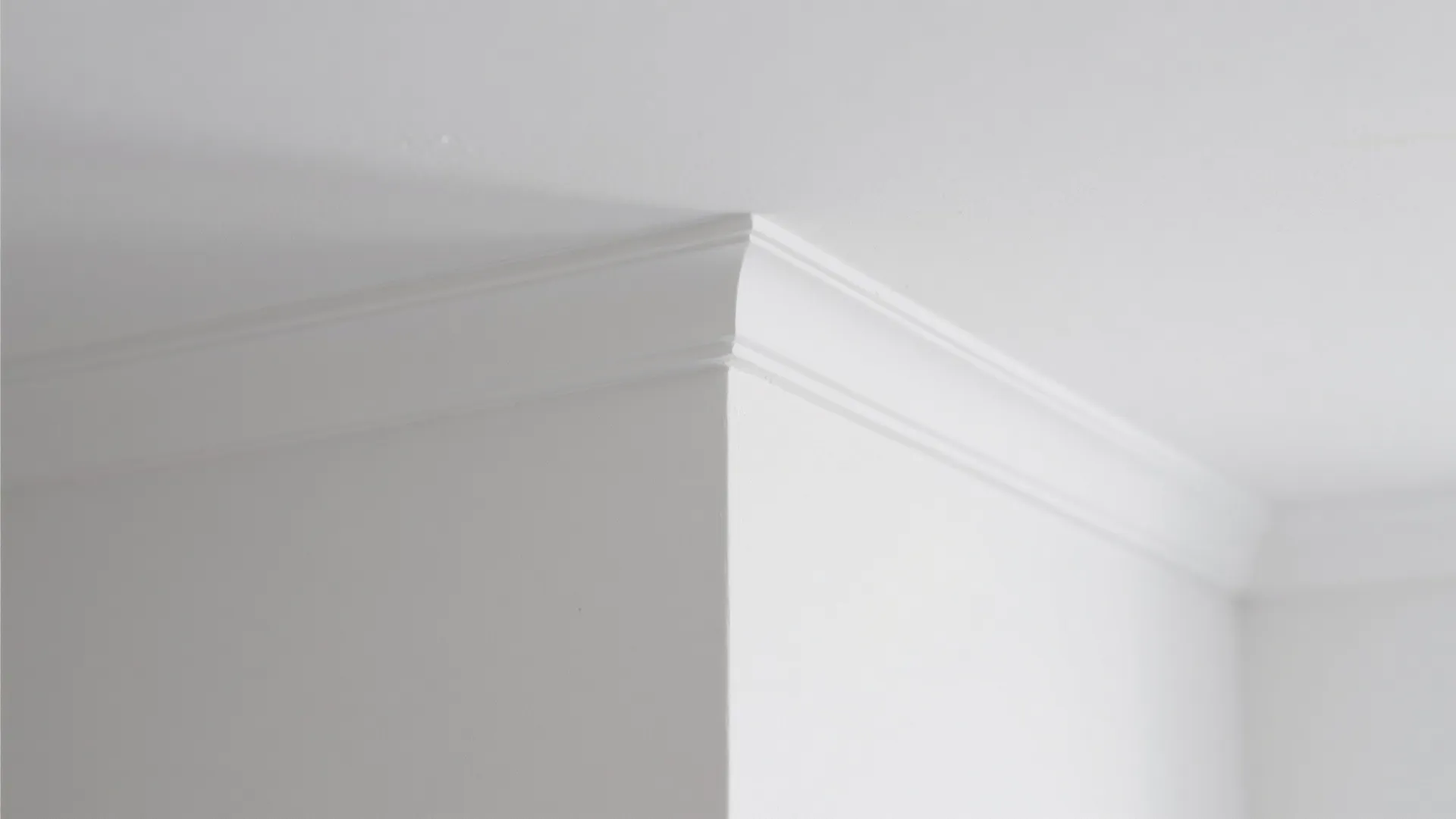 Close up view of white crown molding on a white wall and white ceiling corner