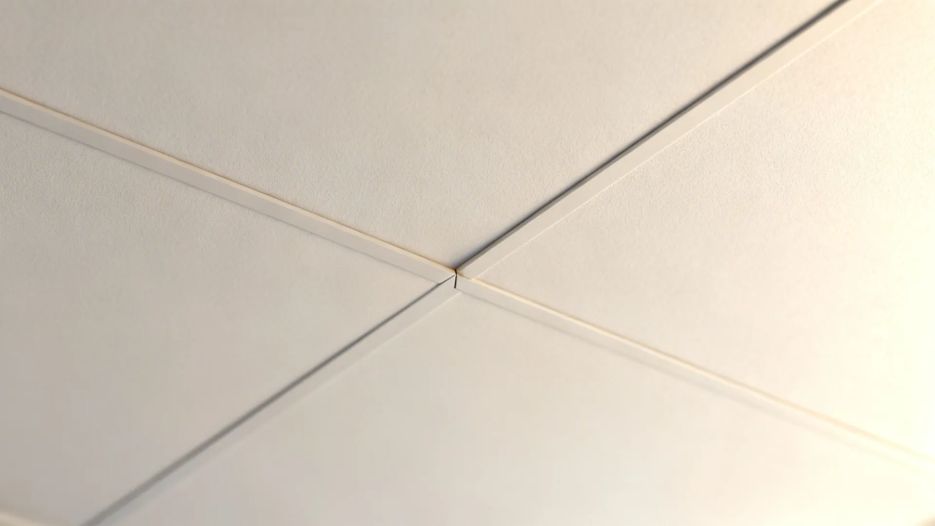 Macro of a PVC ceiling micro-bevel separating warm white and greige panels with a soft shadow.