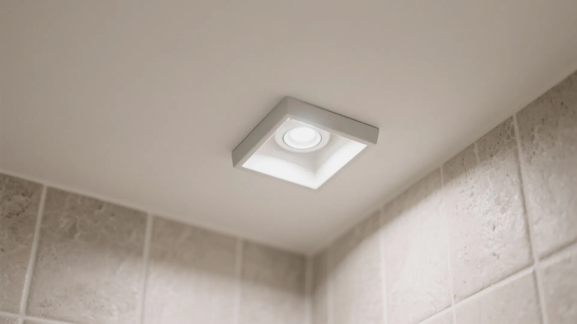 Close up of small square recessed ceiling light fixture installed in white ceiling above wall tiles