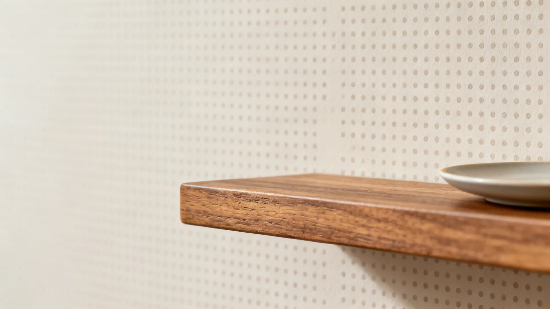 Close-up of crisp tone-on-tone micro-dot stencil behind an oak shelf edge.
