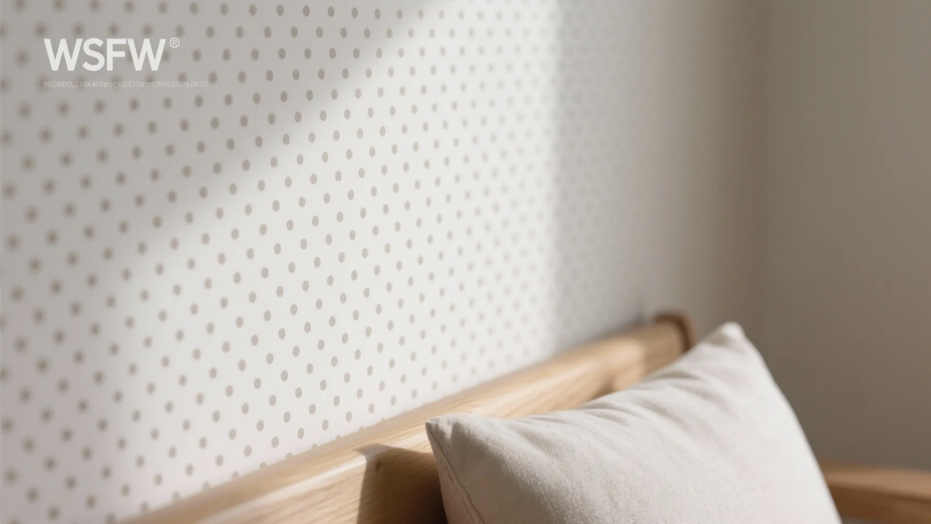 Close up of white wallpaper with grey polka dots behind a wooden bed and pillow