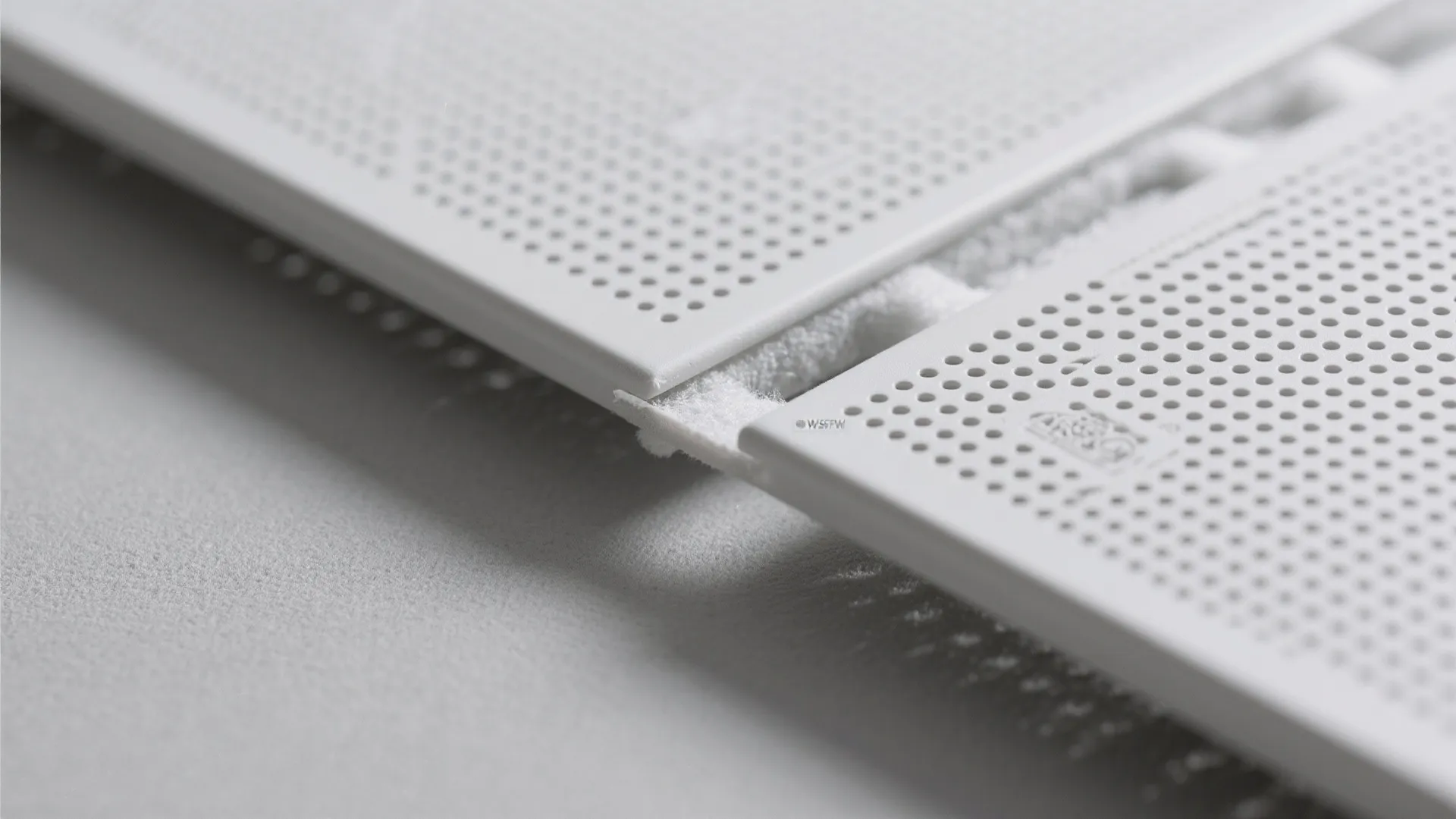 Detailed view of two white metal wall panels with tiny holes connected by joint piece